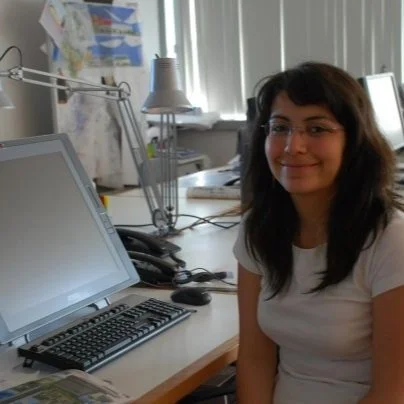 Woman sitting at a desk with a computer and desk lamp in an office setting.