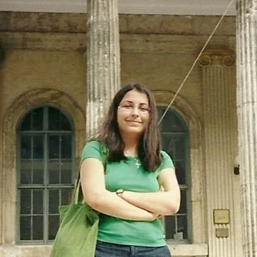 A woman standing with arms crossed in front of historic building with columns.