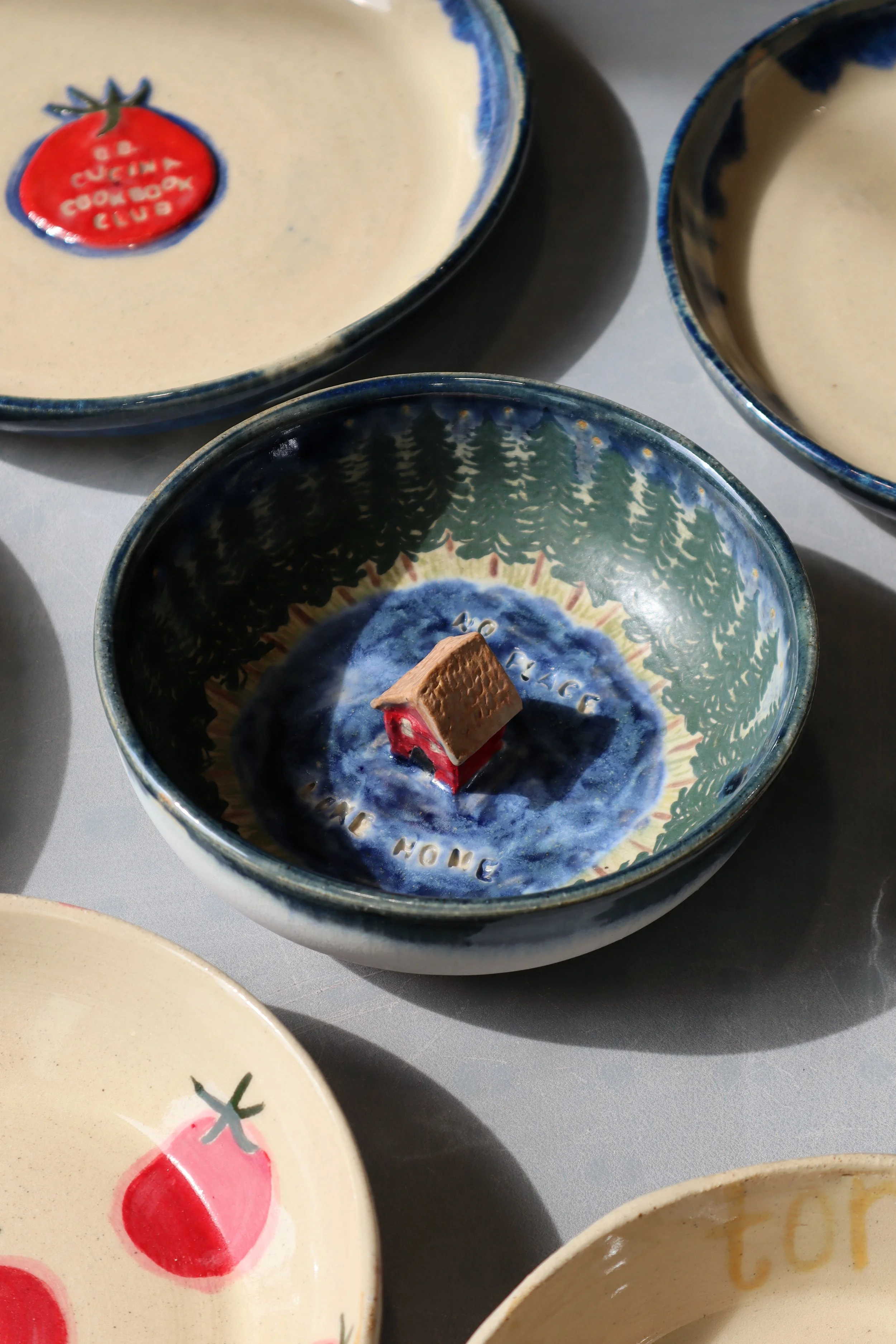 Multiple decorative ceramic bowls with various designs, including a small house figurine inside one bowl, and a bowl with a tomato and strawberry illustration.