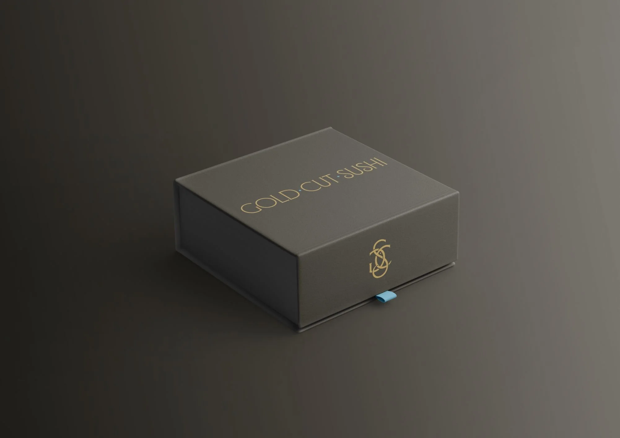A black box with gold lettering that reads 'GOLD CUT-SUSHI' and a gold logo below, placed on a dark surface against a dark background.