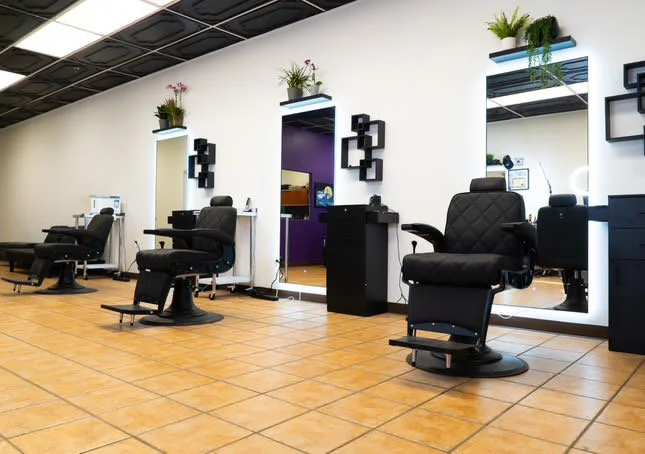	
Interior of a modern barber shop xternalstudio located in clovis CA with black chairs, mirrors, and wall-mounted shelves with plants.