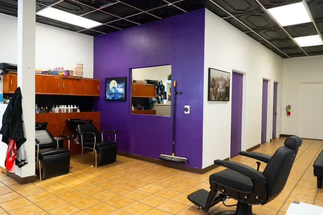 nterior of a modern barber shop xternalstudio located in clovis CApurple accent walls, wall mirrors, and wooden cabinets holding hair products. Ceramic tiled floor and fluorescent ceiling lighting.