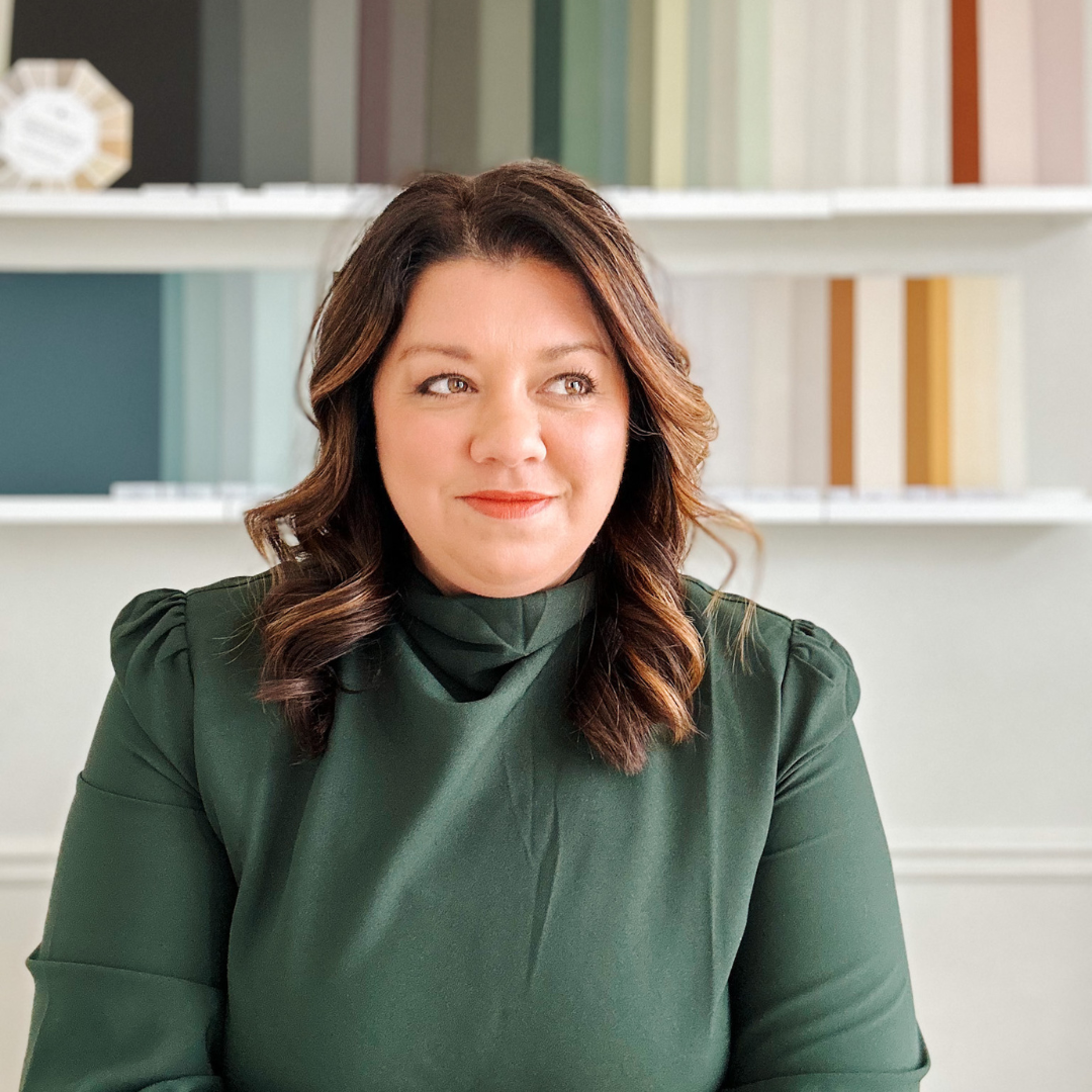 Woman in green blouse, with wavy hair, smiles gently against a backdrop of vertical fabric rolls.