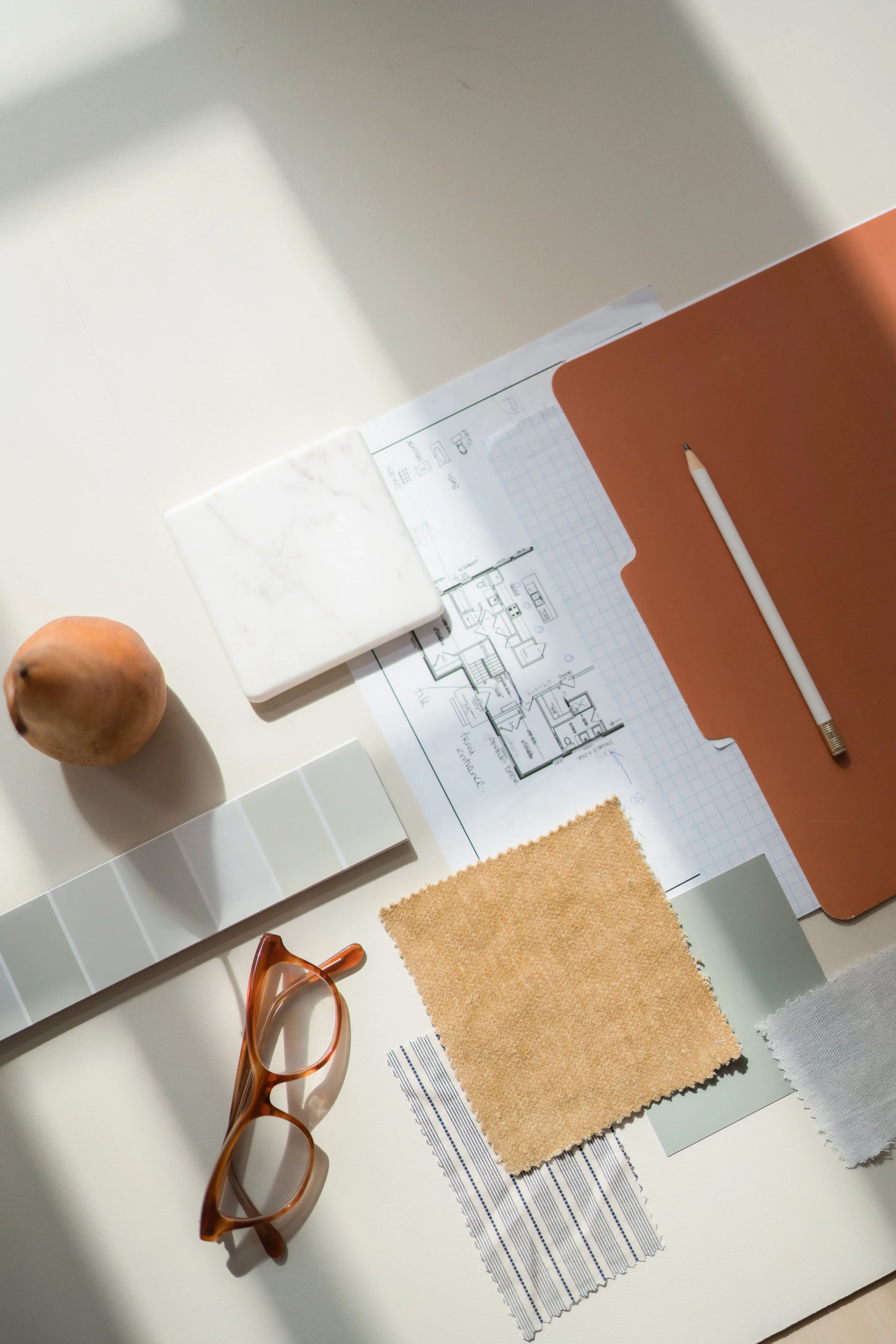 Overhead view of a desk with red glasses, a pencil, architectural plans, and a fabric swatch.