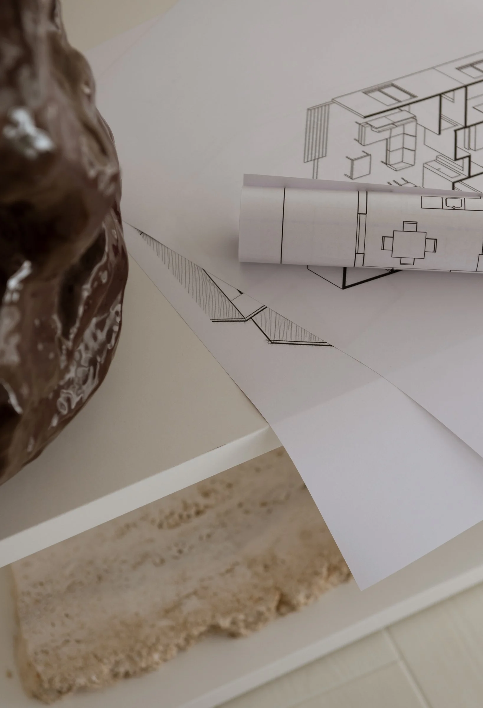 A close-up of architectural drawings on white paper, with part of a brown object on the left side of the picture.