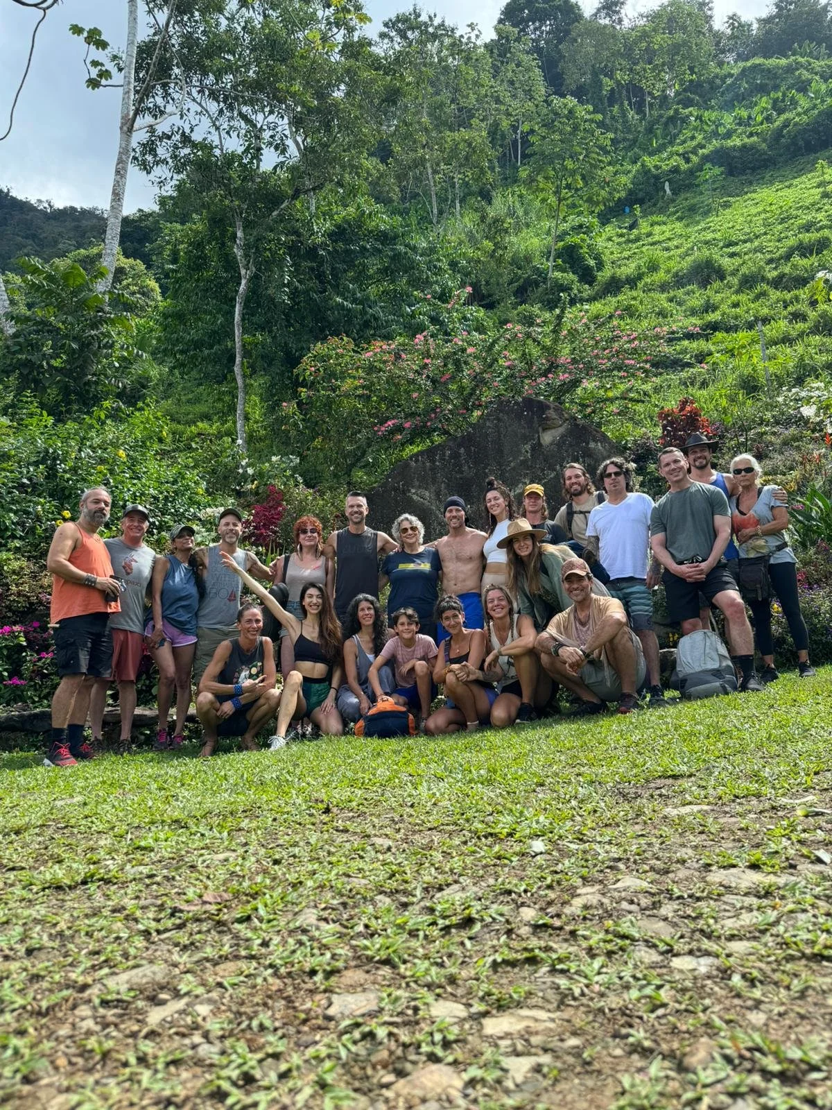 A group of people posing for a photo outdoors in a lush, green, hilly environment with dense trees and flowering plants.