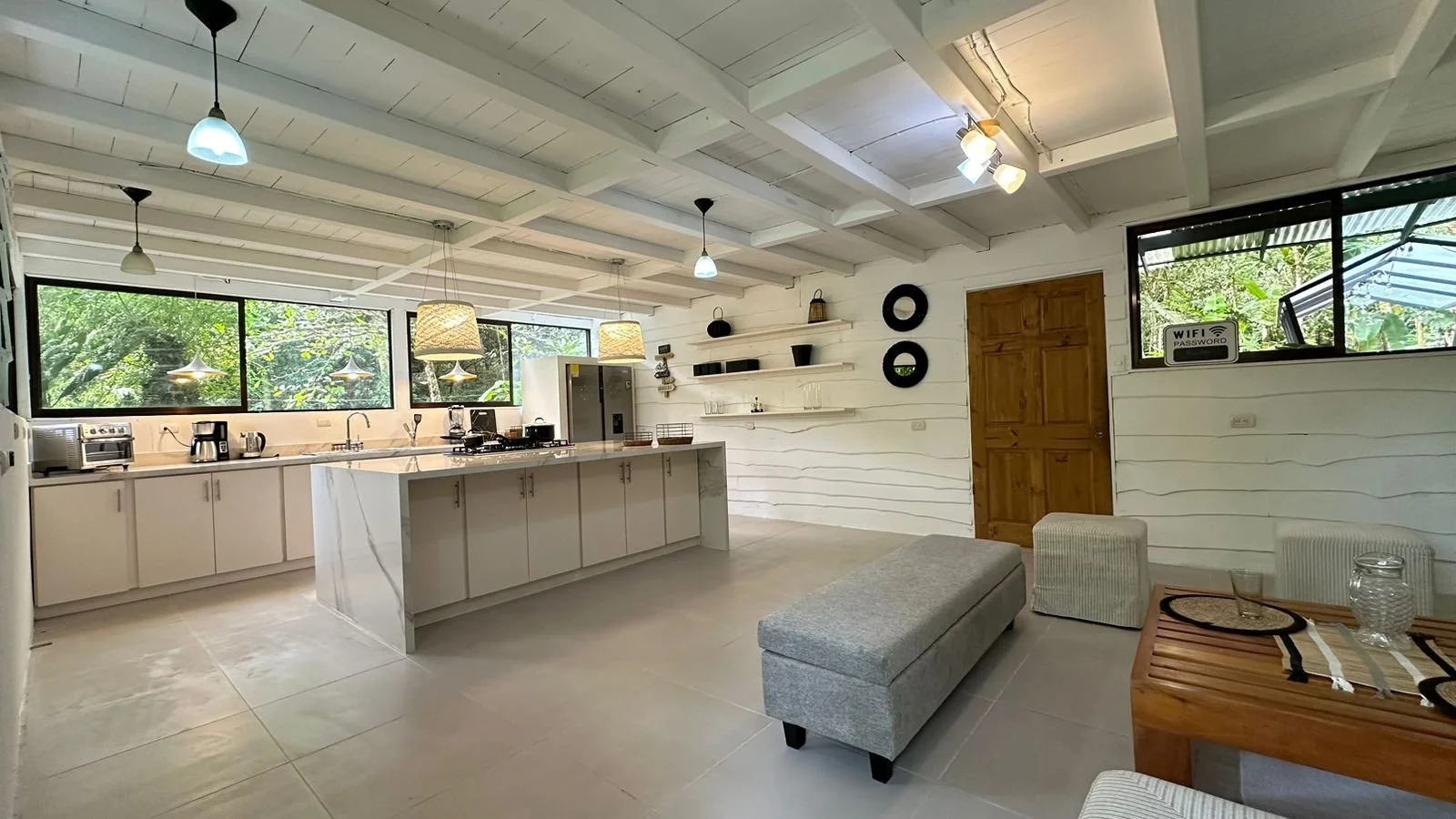 Modern kitchen and living area with large windows, white cabinets, wooden door, and minimal decor.