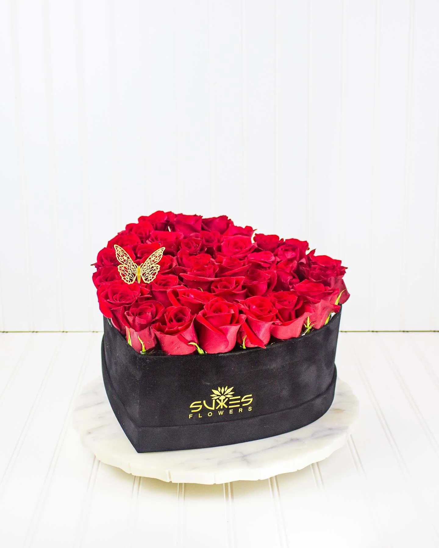 A timeless statement of love and passion &mdash; lush red roses arranged in a black velvet heart box, finished with a golden butterfly touch. Perfect for when words aren&rsquo;t enough.