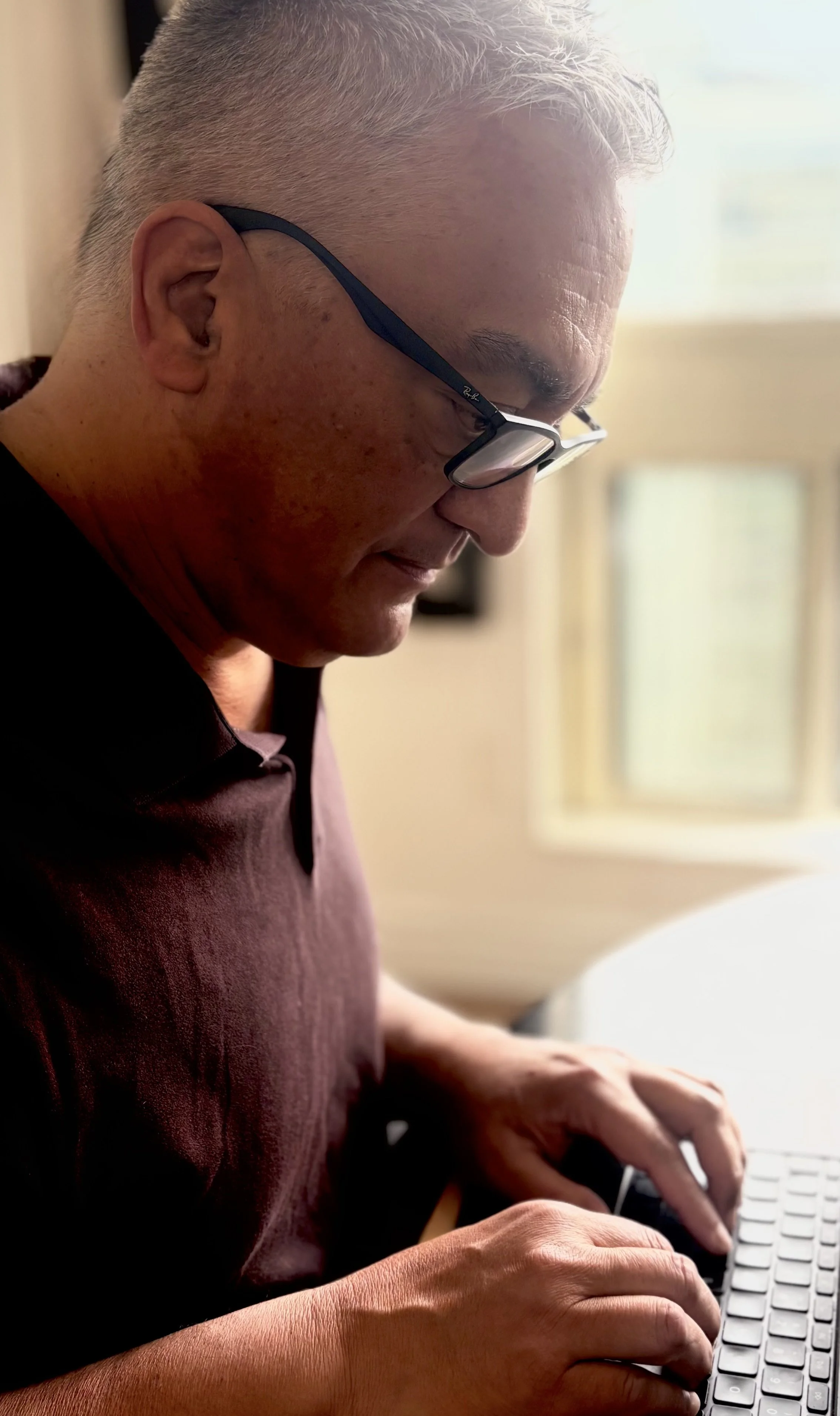 A man with glasses typing on a computer keyboard.