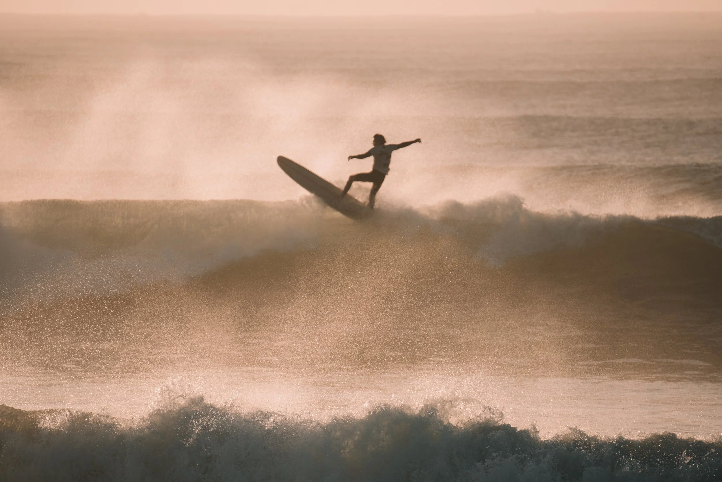 A person surfing on a wave at sunset, balancing on the surfboard with arms outstretched.