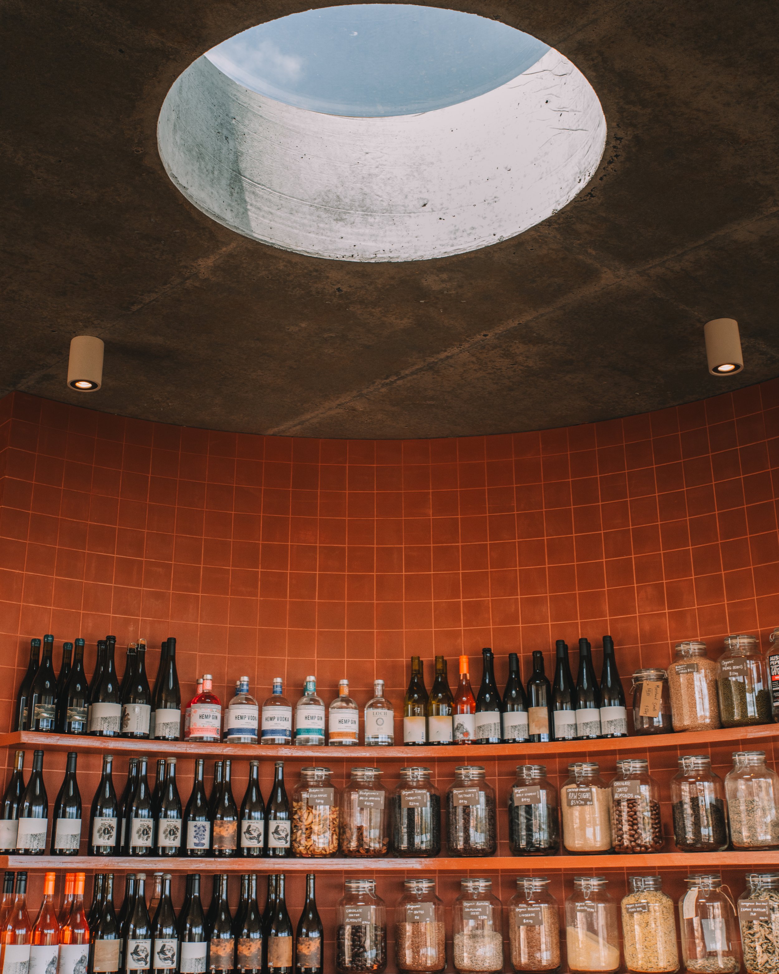 Interior of a shop with shelves of bottles and jars, a circular skylight in the ceiling, and red tile walls.