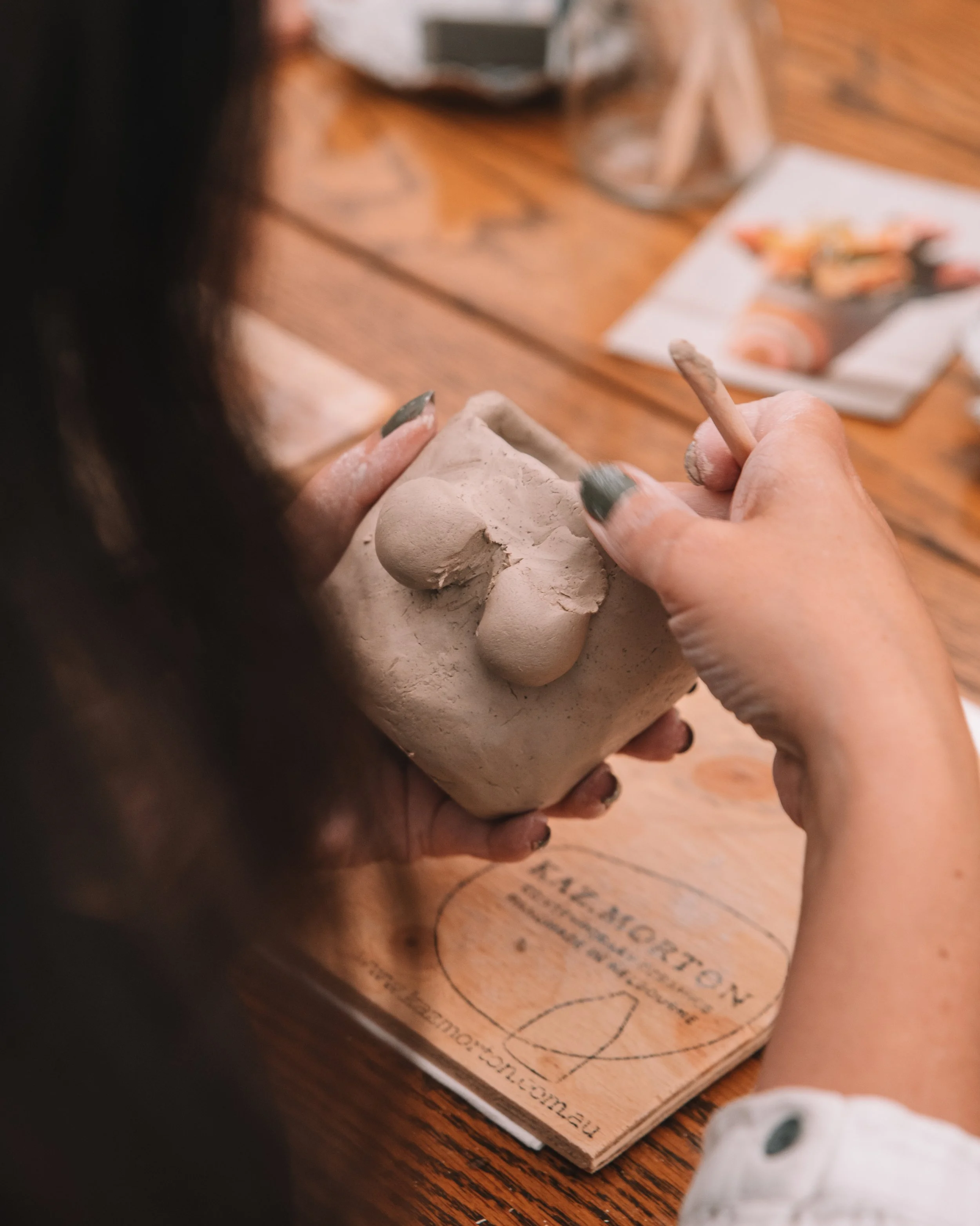 Person carving a clay sculpture with tools at a wooden table.