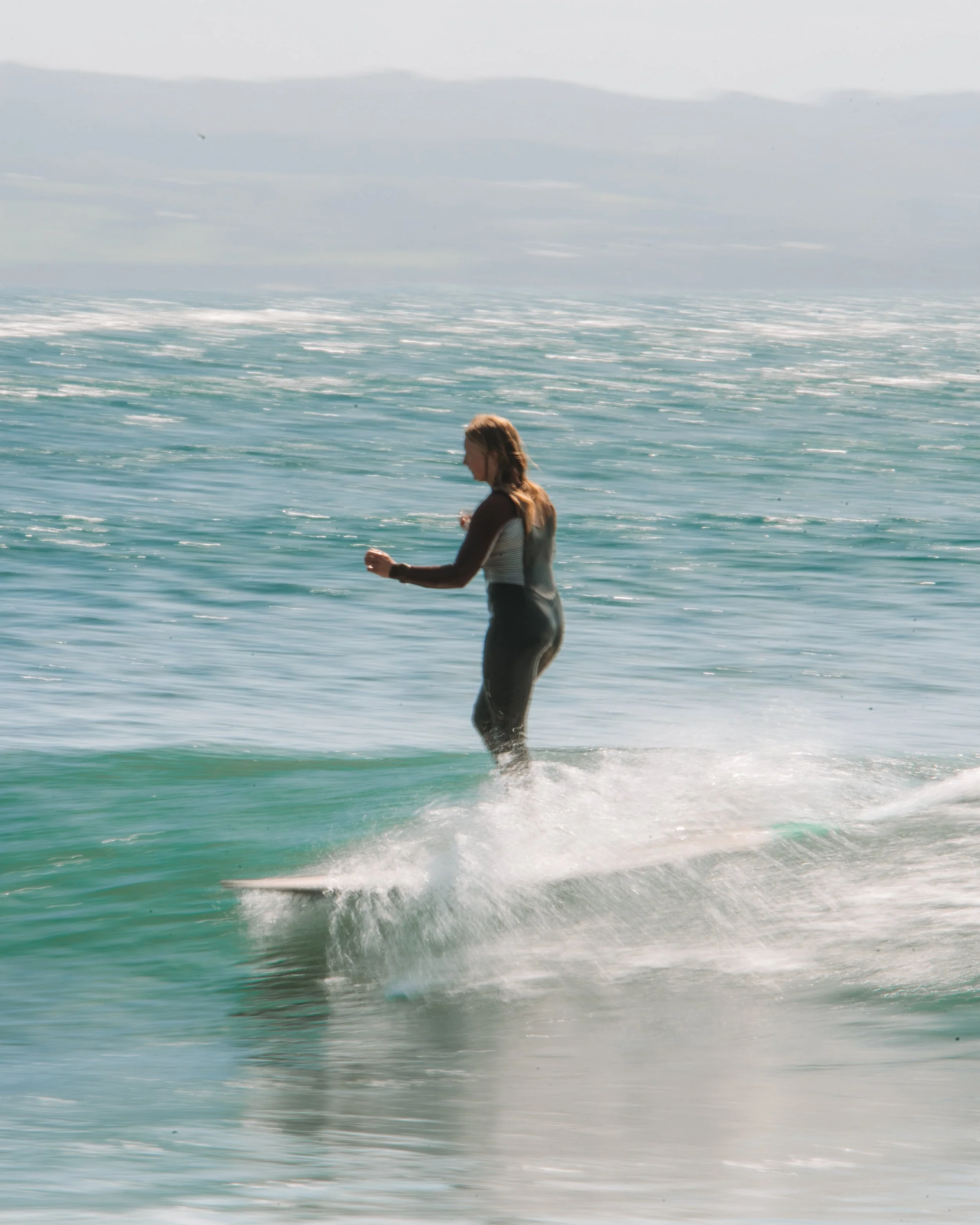 A woman surfing on a small wave in the ocean, wearing a wetsuit.