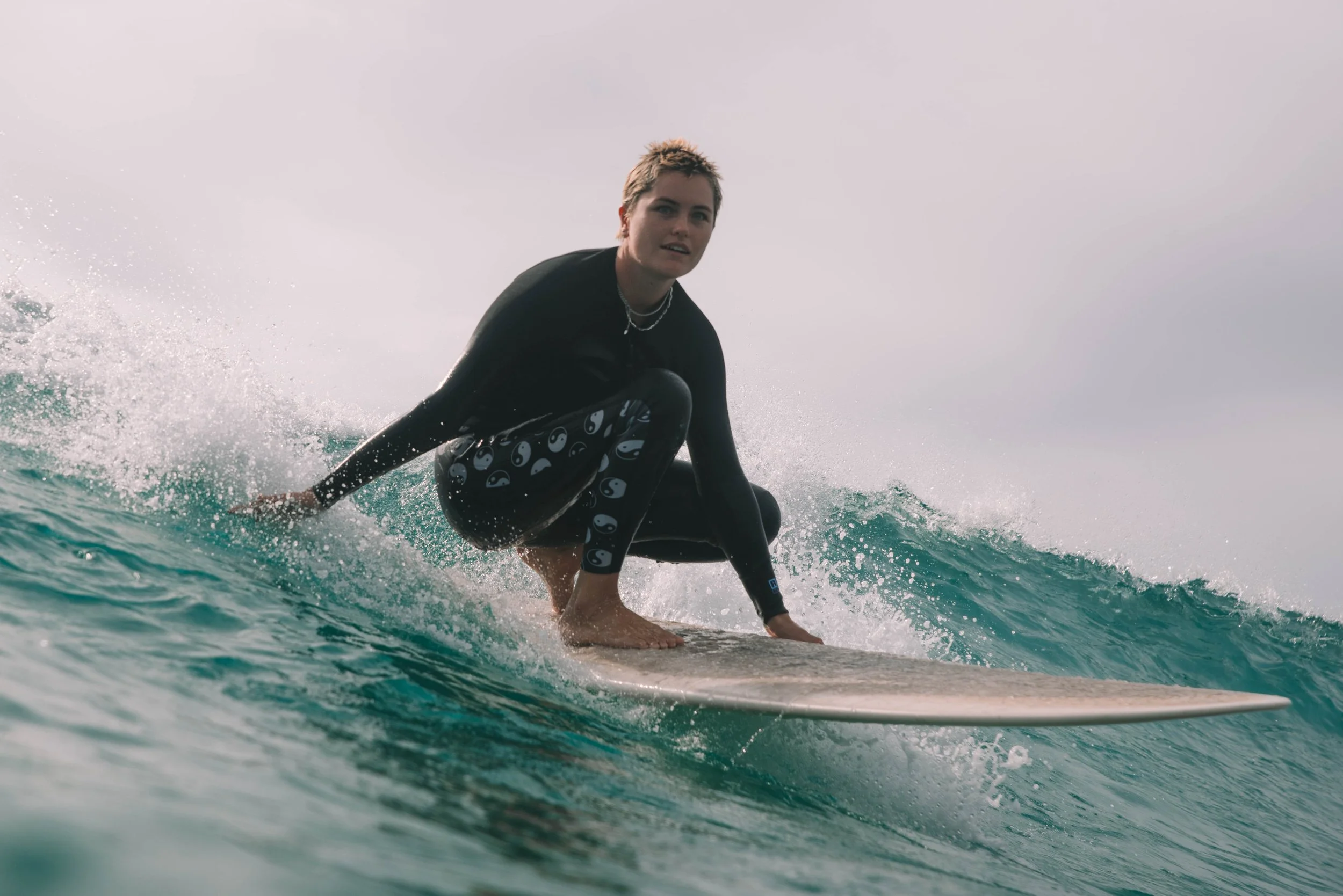 Person surfing on a wave in the ocean, wearing a black wetsuit with yin-yang symbols.