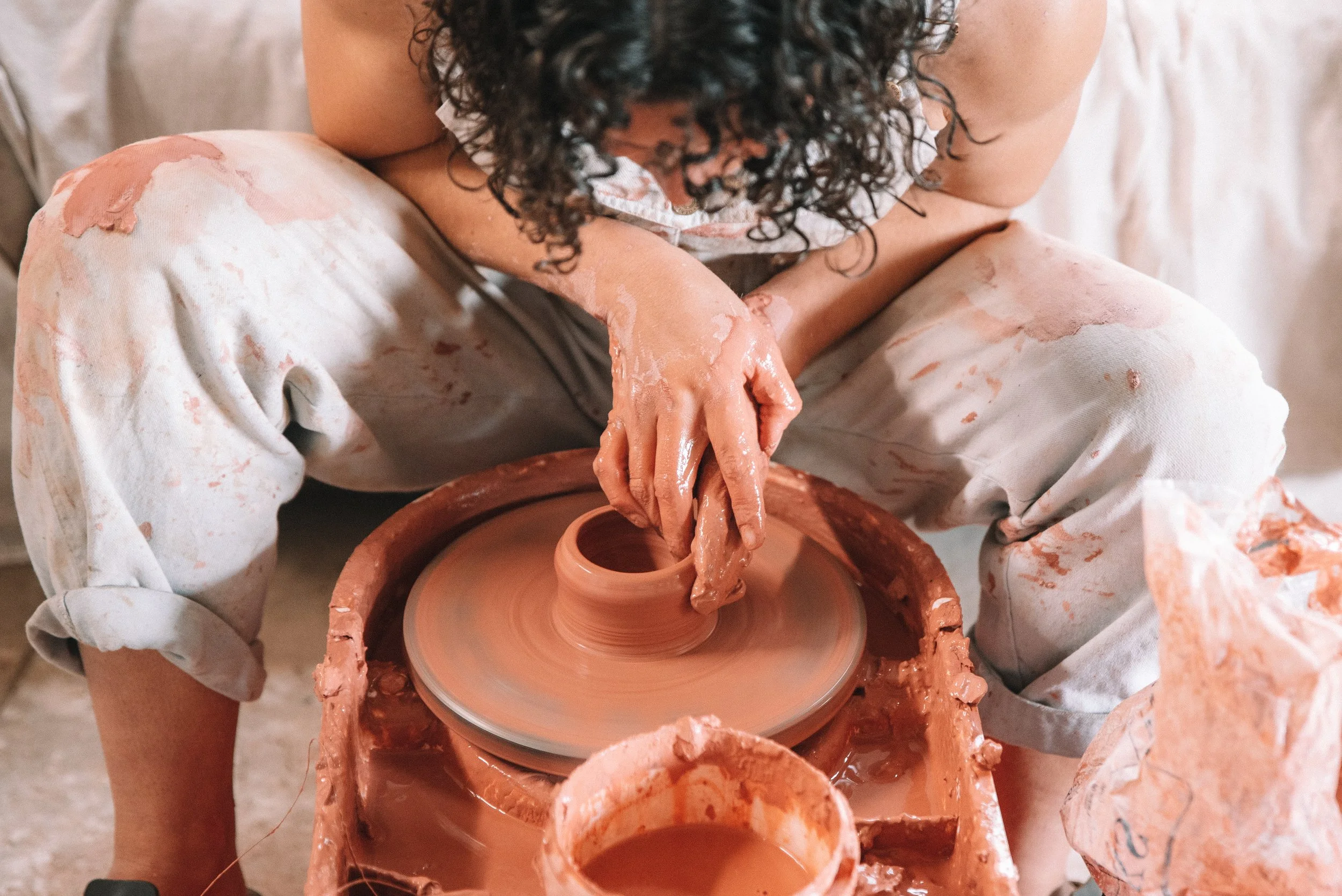 Person molding clay on a pottery wheel with their hands