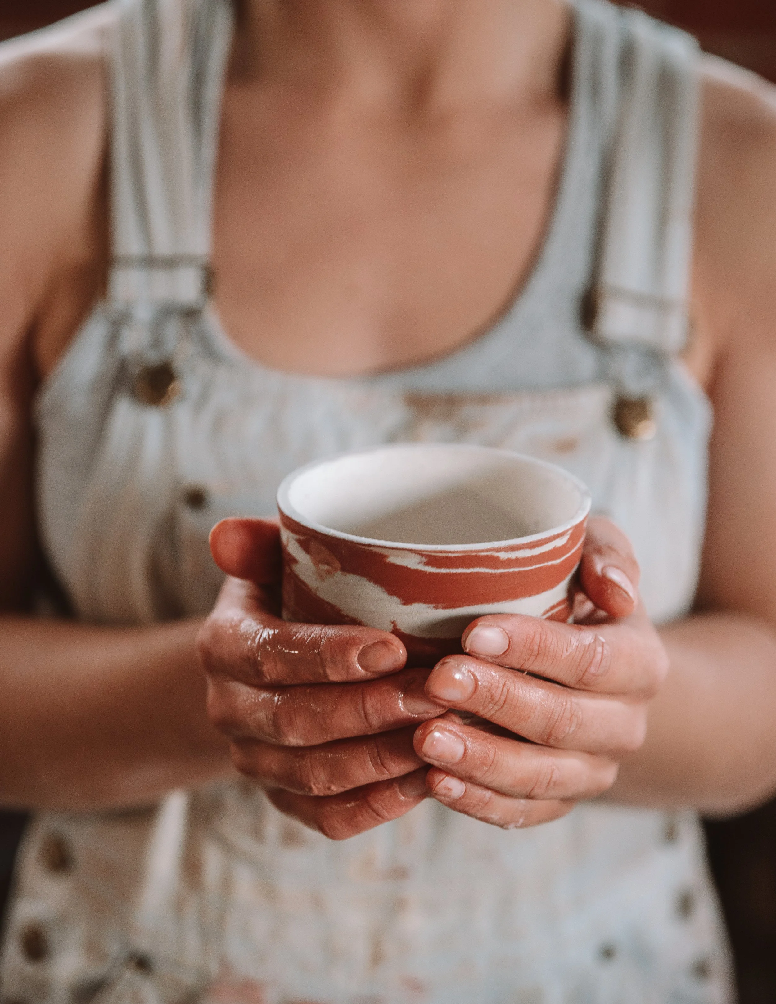 Person holding a ceramic mug with a marbled orange and white pattern, wearing a white sleeveless top.