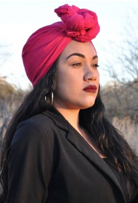 A woman standing while wearing a red headscarf and black blazer.