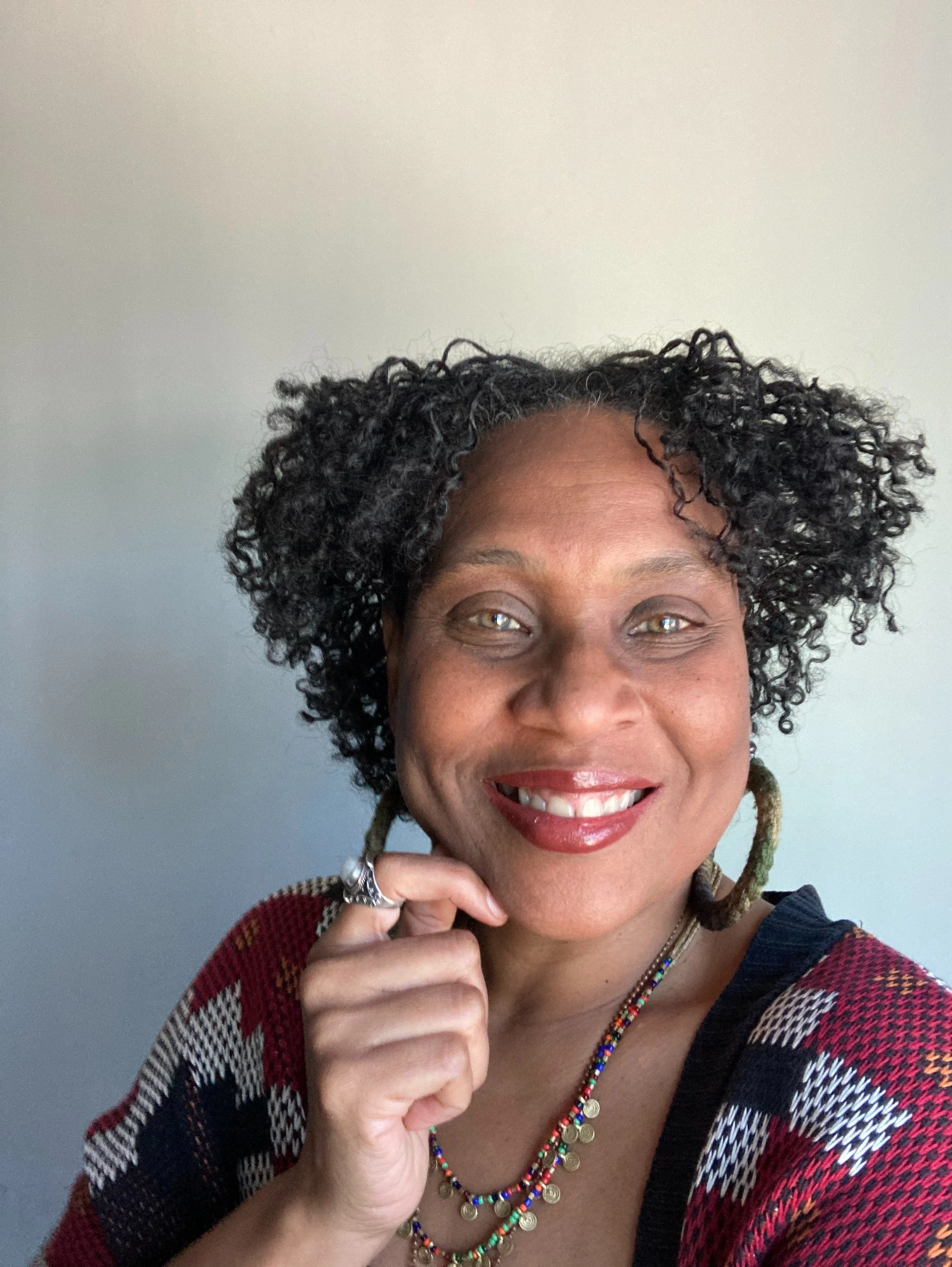 A woman with curly hair smiles and wears a red lipstick.