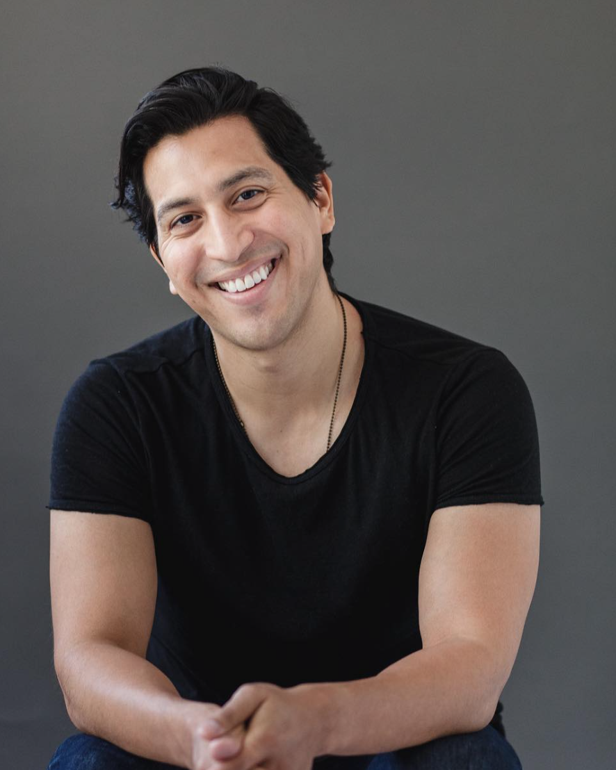 A man with a black v-neck tee shirt smiles broadly into the camera.