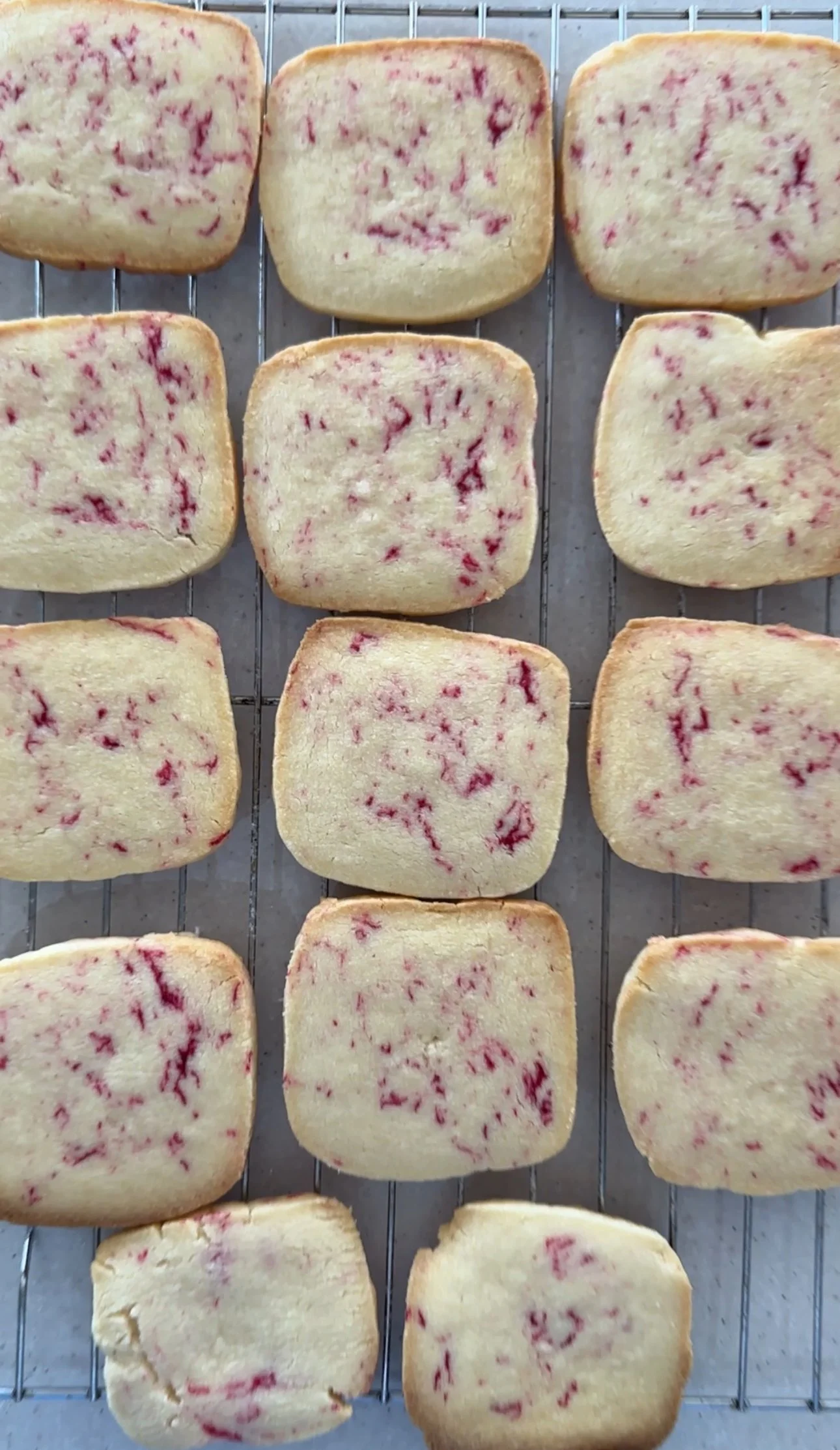 Frosted pastries with raspberry topping on a cooling rack.
