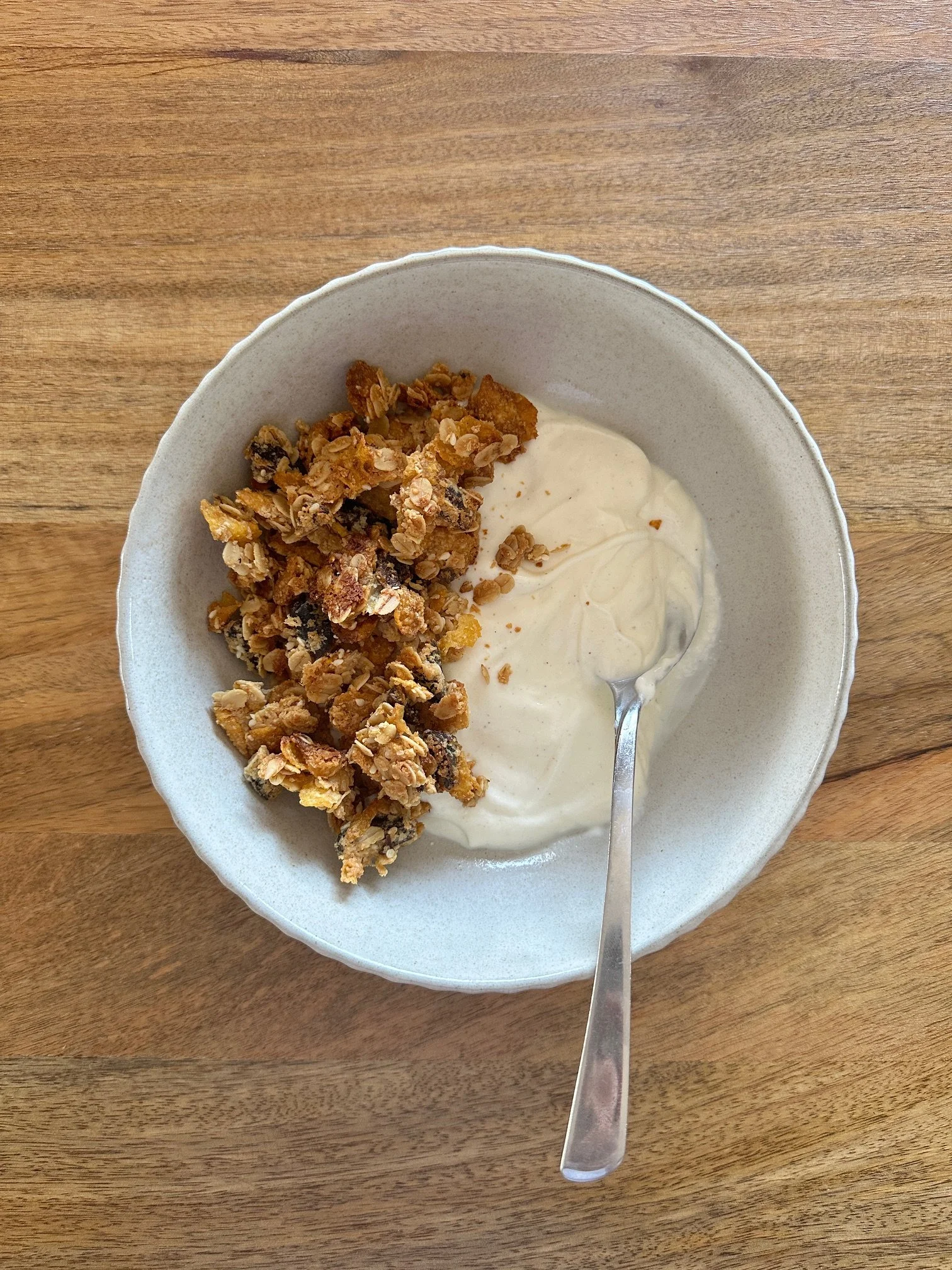 A bowl containing granola and yogurt on a wooden surface with a spoon.