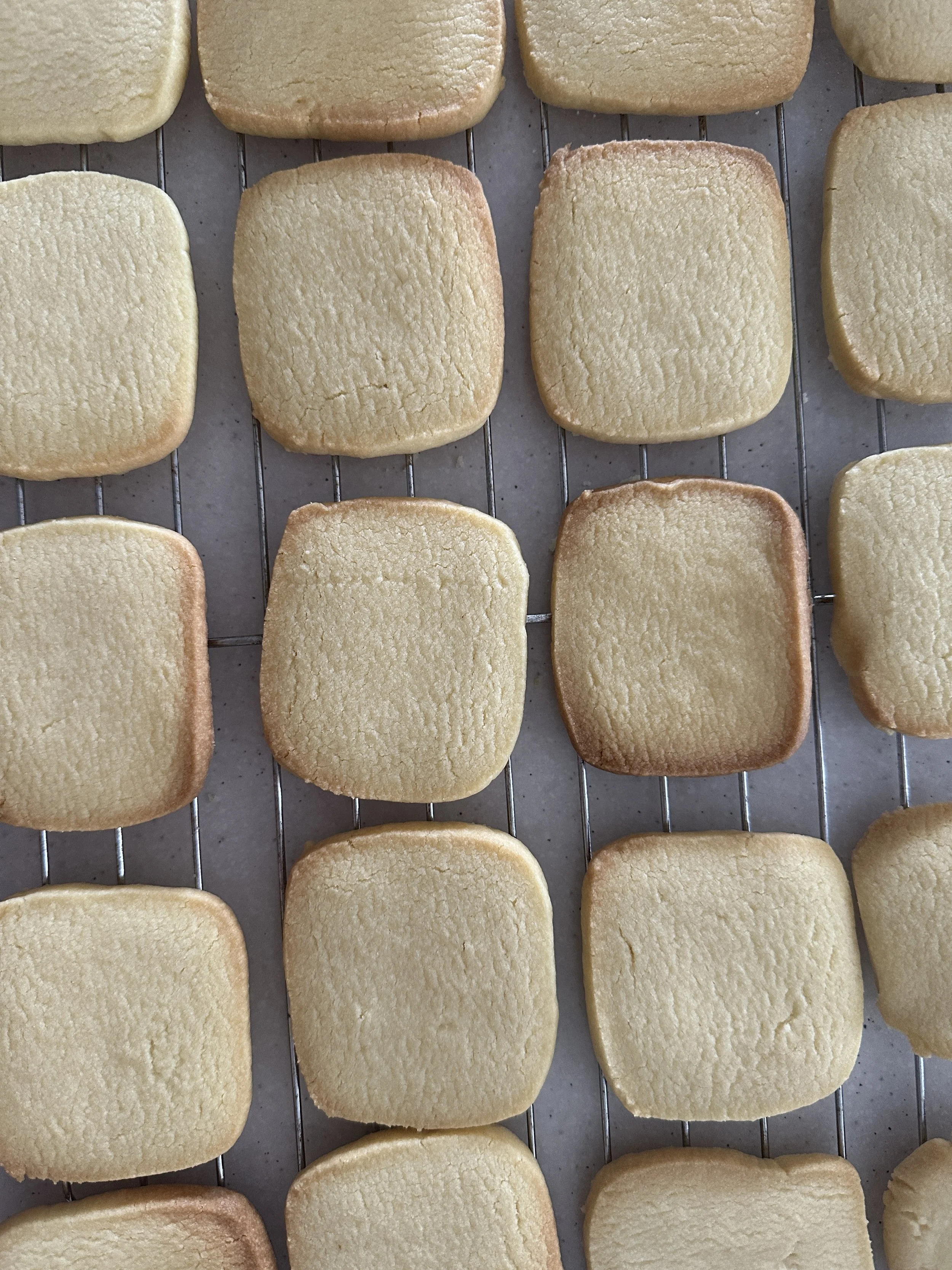 Arranged on a cooling rack are freshly baked, square-shaped sugar cookies with slightly rounded edges, golden-brown on the sides and lighter in the center.