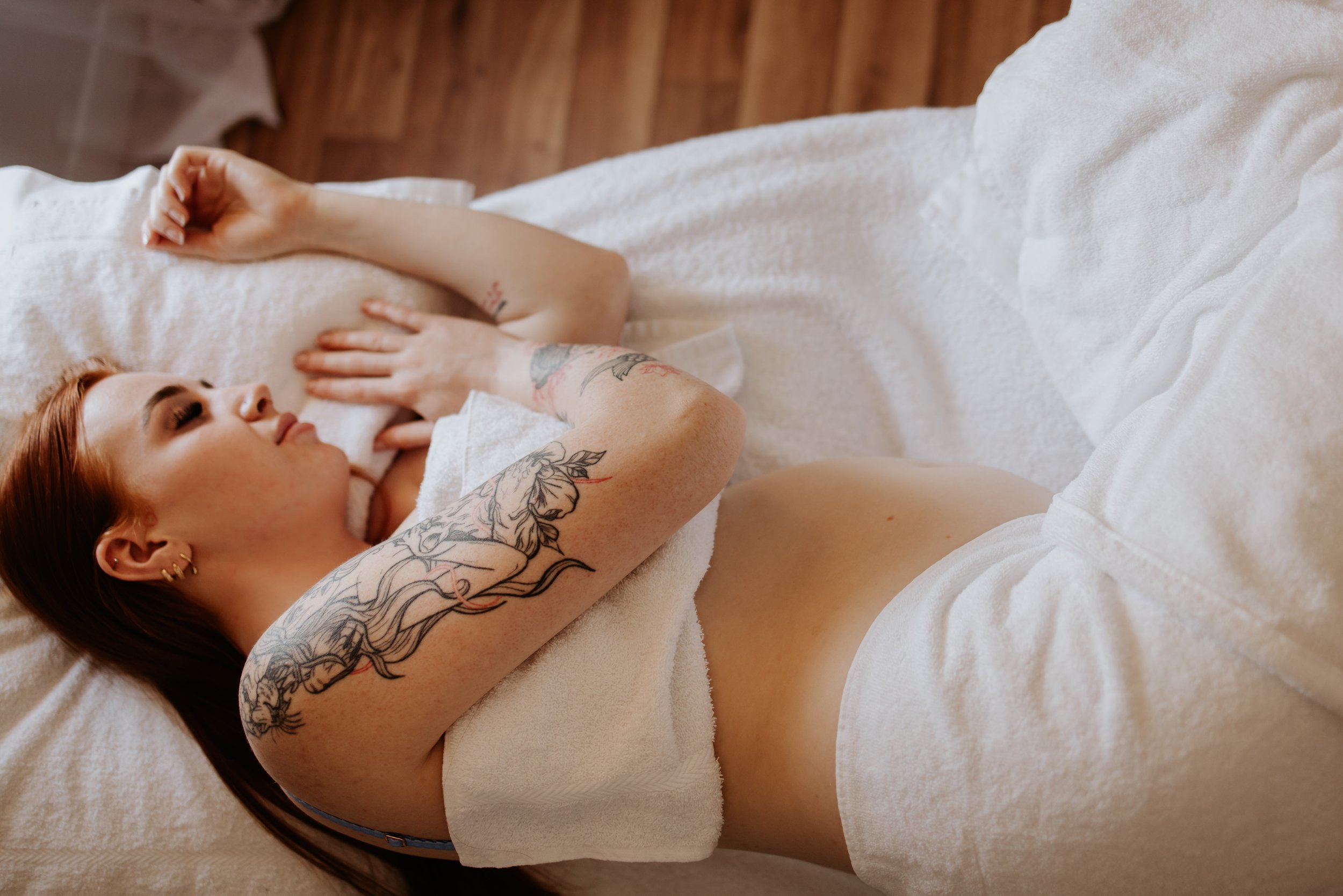 Person with tattoos on arm lying on a bed covered with white towels, resting.