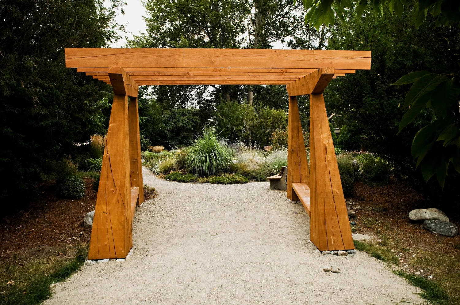 The cedar archway at the entrance to the Sacred Garden, with a gravel path leading into the plantings