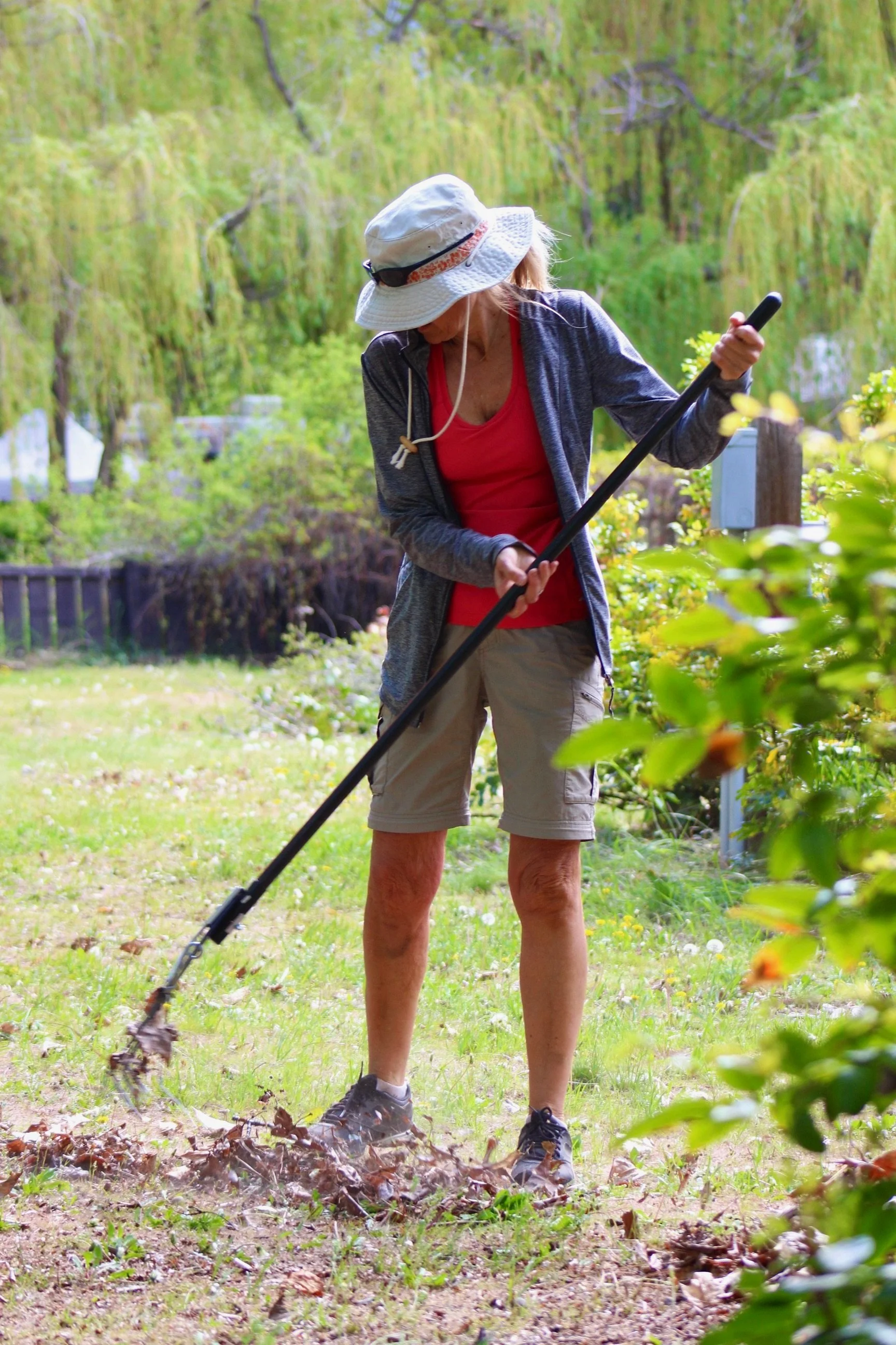 A woman raking leaves in a backyard garden during the day.