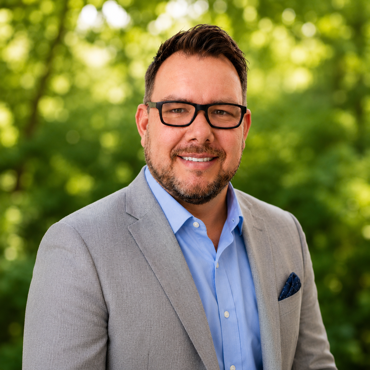 Peter is smiling wearing dark rimmed glasses and a light grey suit jacked