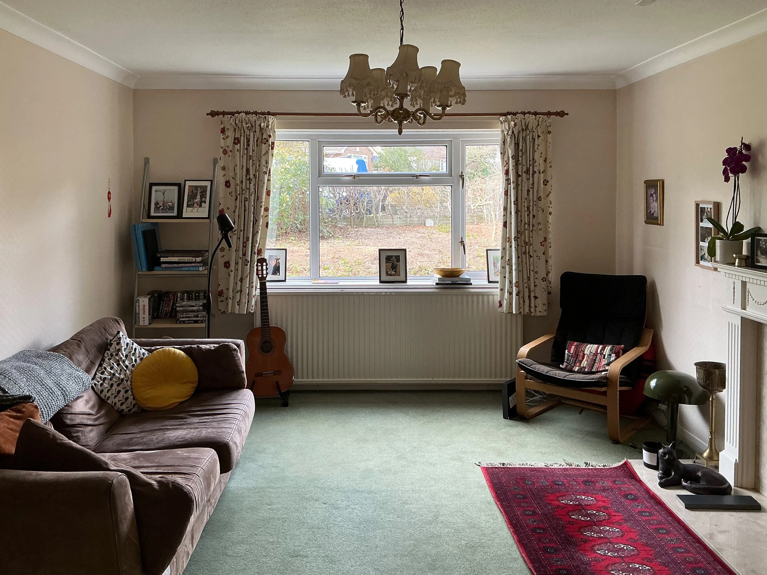 A photo of a living room with a green carpet, brown sofa and red patterned rug in front of a fireplace