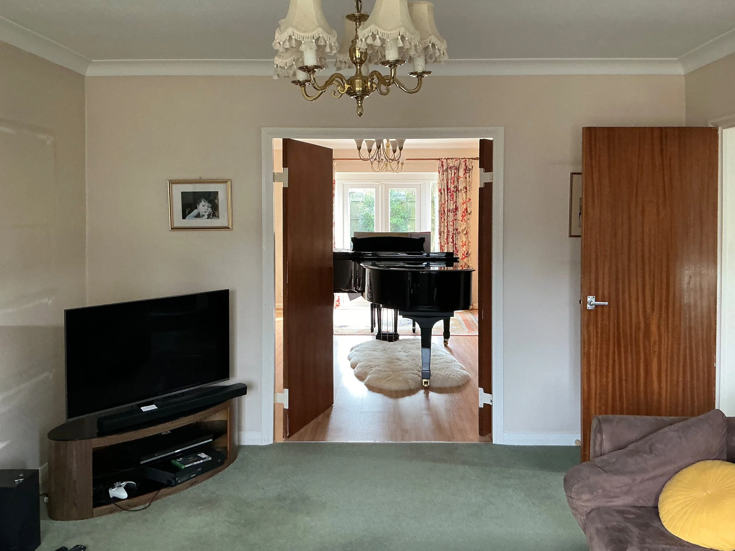 A photograph of a living room with central double doors leading to a piano room, with a grand piano