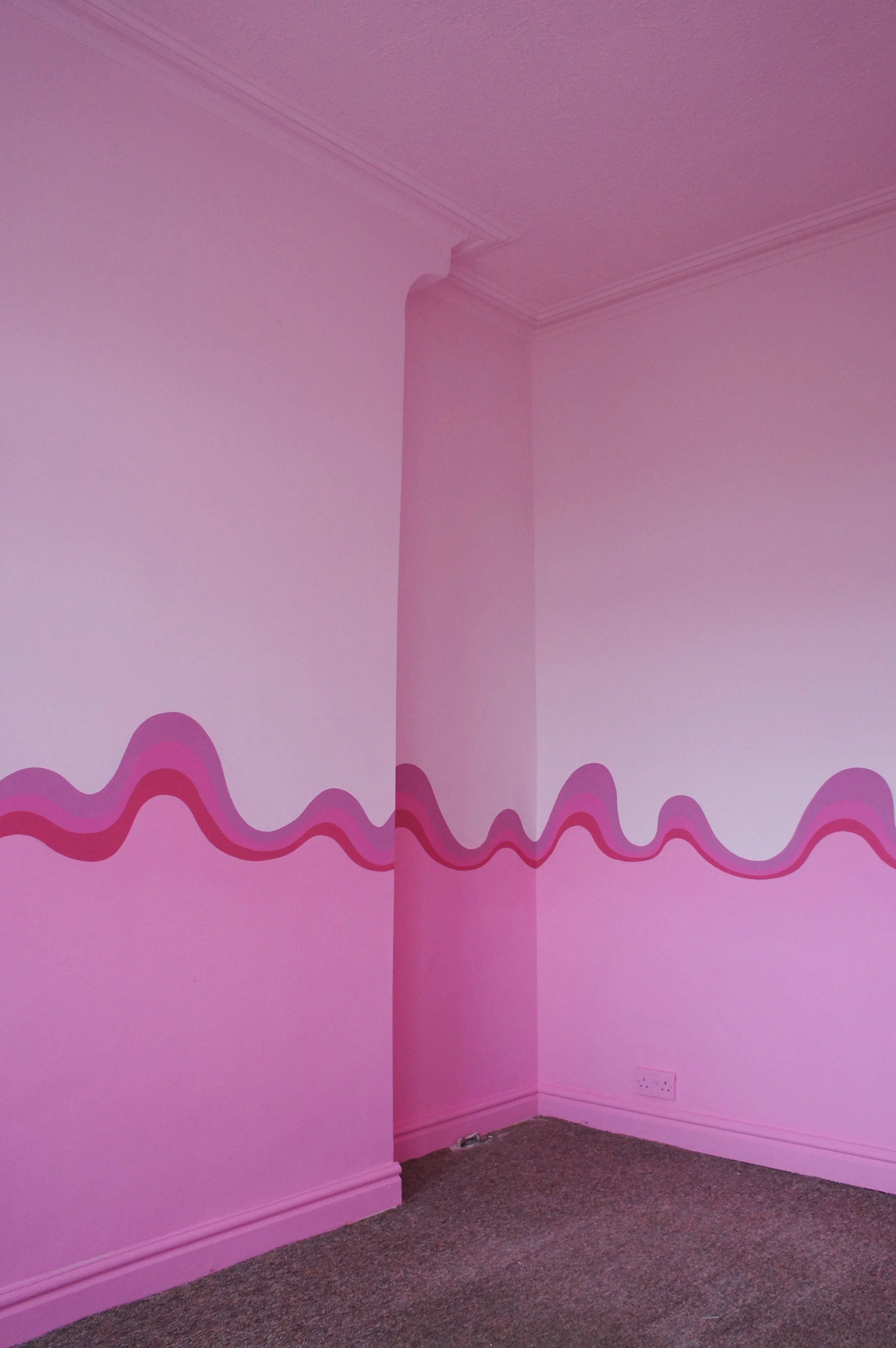 In a pink themed bedroom a swirly stripe of differing shades of pink wiggles across the chimney breast, alcoves and walls