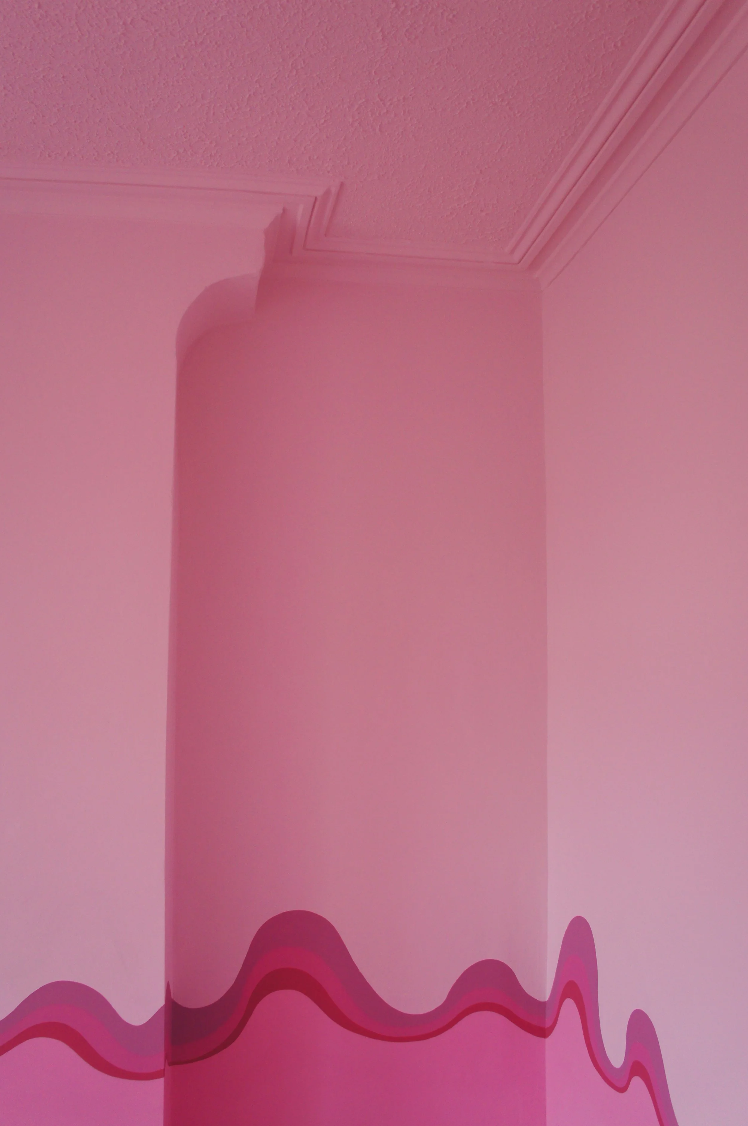 An alcove of a bedroom painted pink with a swirly stripe at dado height