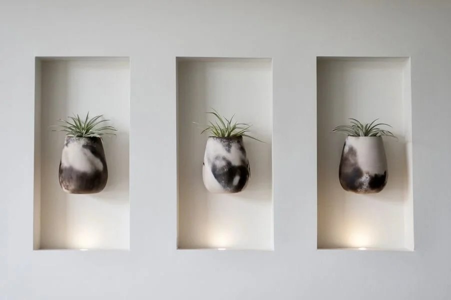 Rachael Goddard Design Studio Calabasas Three wall-mounted planters with green plants in black and white marbled pots in recessed wall niches.