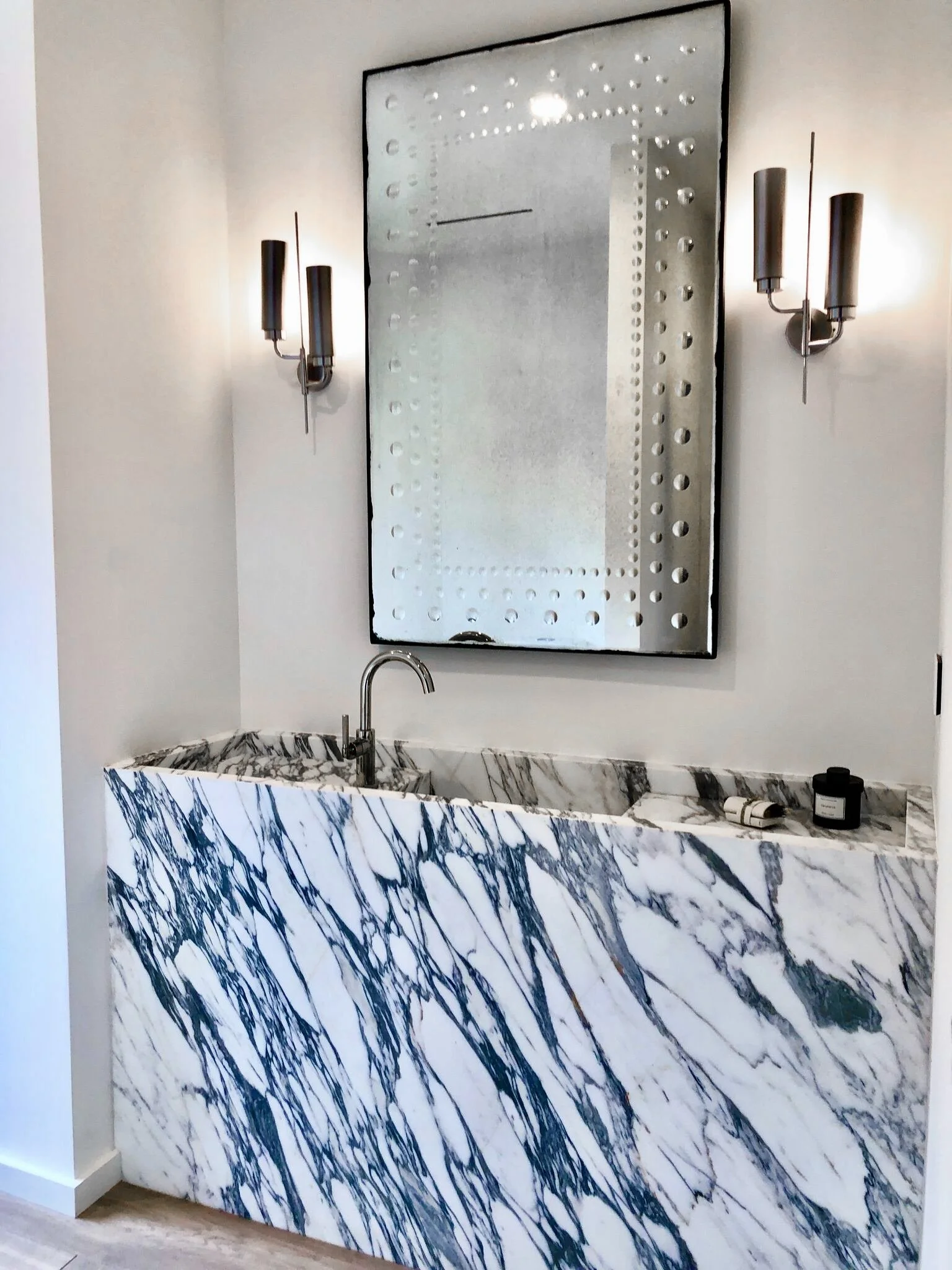 Bathroom with a marble sink, wall-mounted mirror, and wall sconces.  Rachael Goddard Design Studio Calabasas
