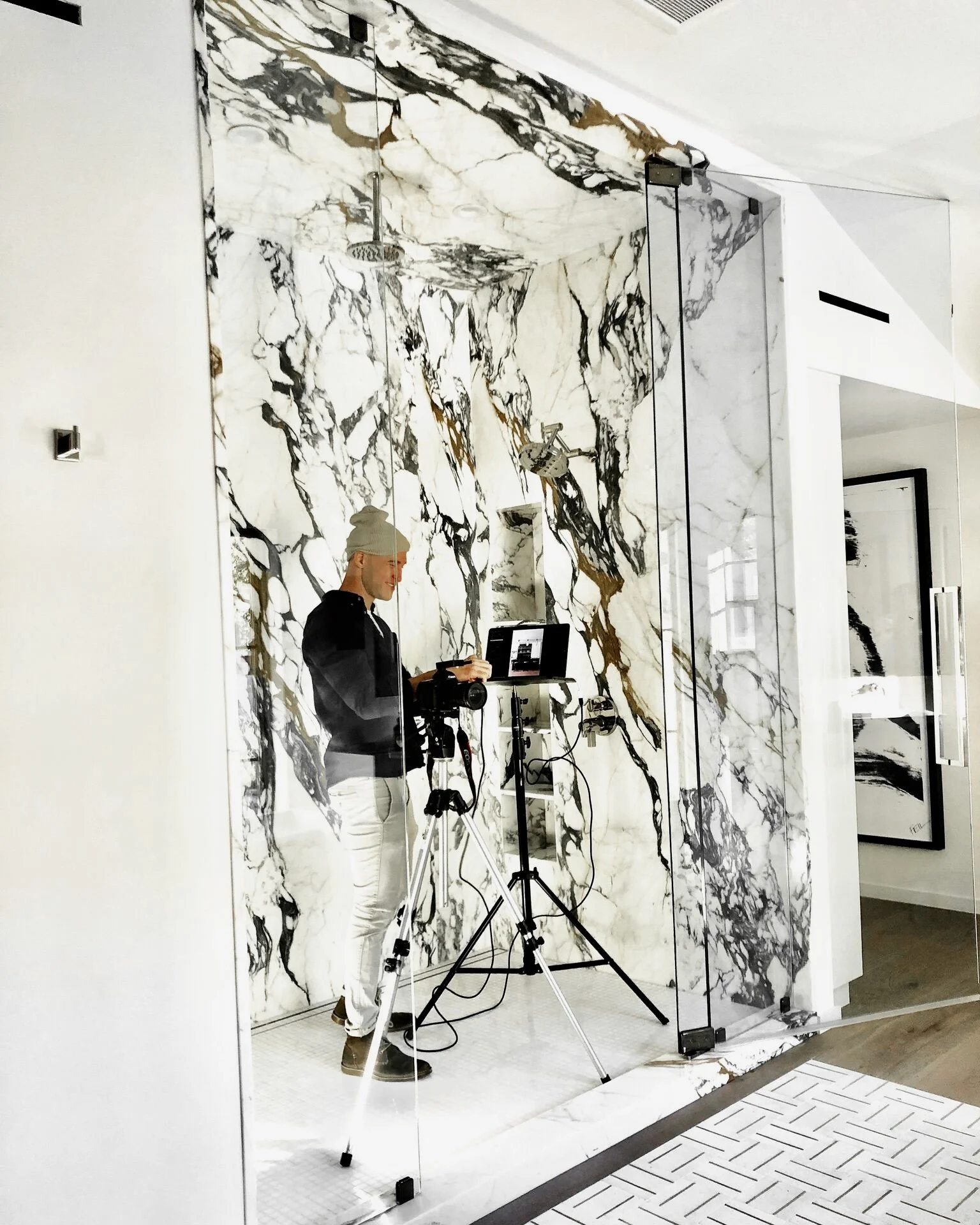Person with a camera and tripod in front of a marble wall, taking photographs in a modern interior space. Rachael Goddard Design Studio Calabasas