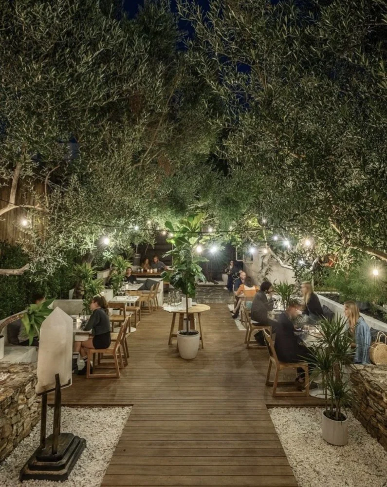 Rachael Goddard Design Studio Calabasas Evening view of an outdoor dining area with trees and string lights, with people sitting at tables enjoying meals.