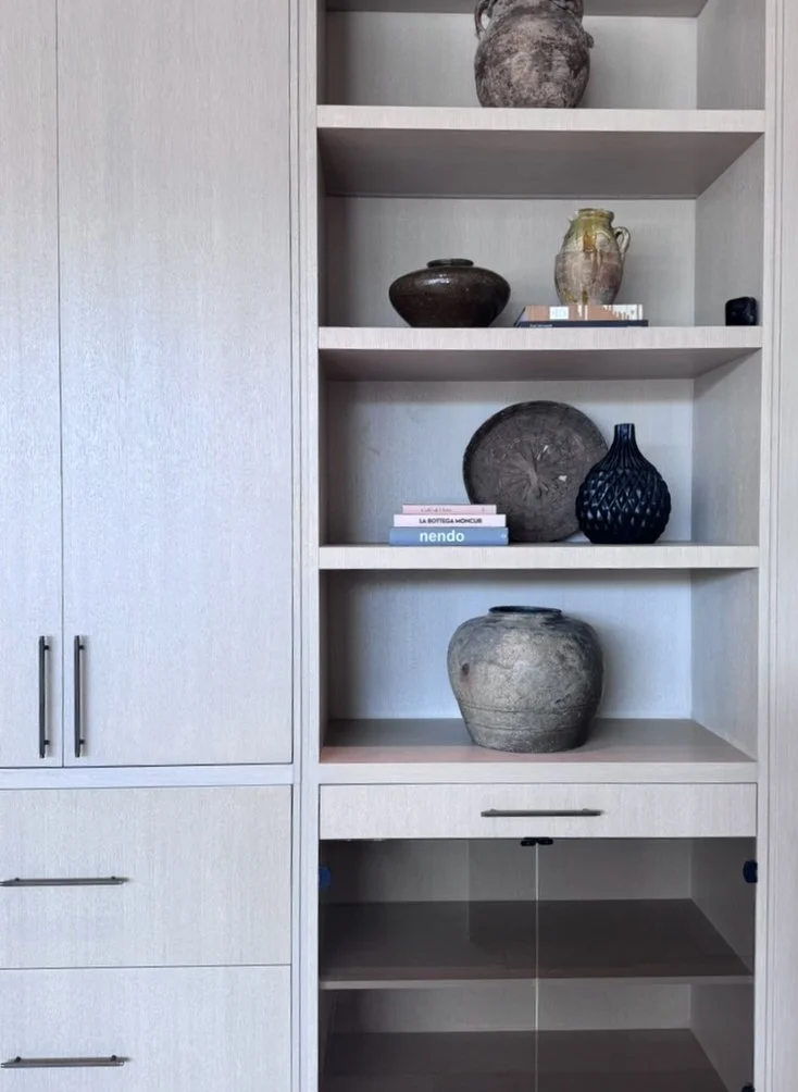 Rachael Goddard Design Studio Calabasas Built-in shelving unit with various ceramic vases and decorative objects, including a stack of books, set against a light gray wall.