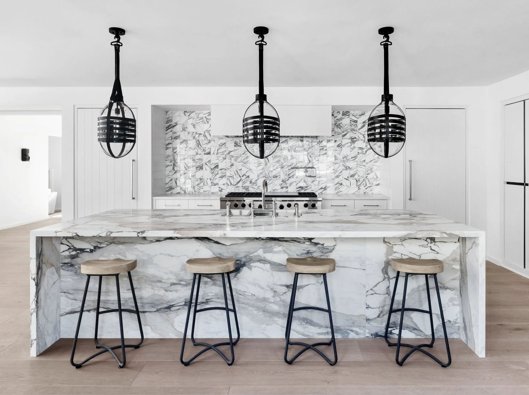 Modern kitchen with white marble island, black hanging pendant lights, and a marble backsplash.