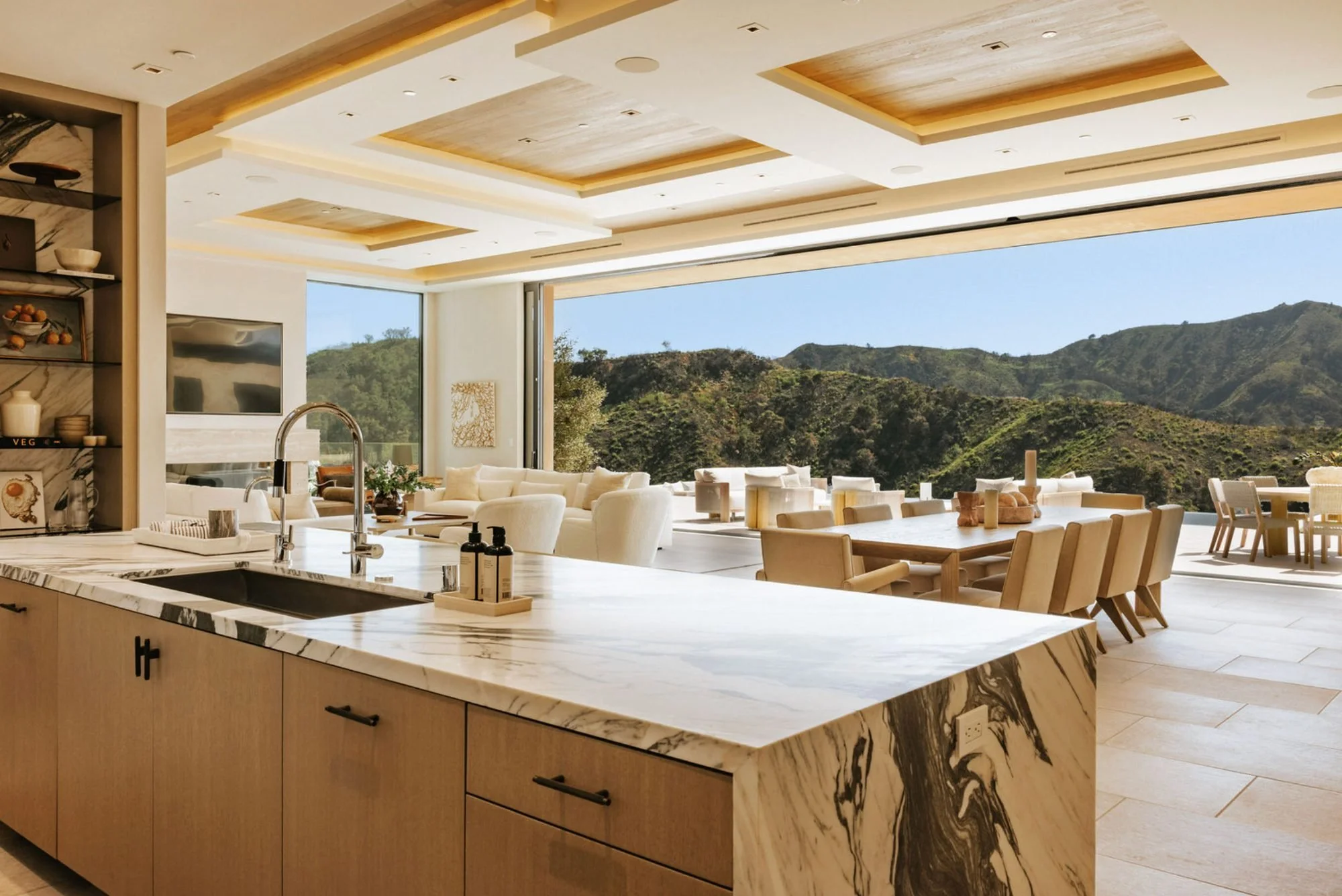 Rachael Goddard Design Studio Calabasas Modern kitchen and dining area with open view of green hills, white furniture, and a marble kitchen island.