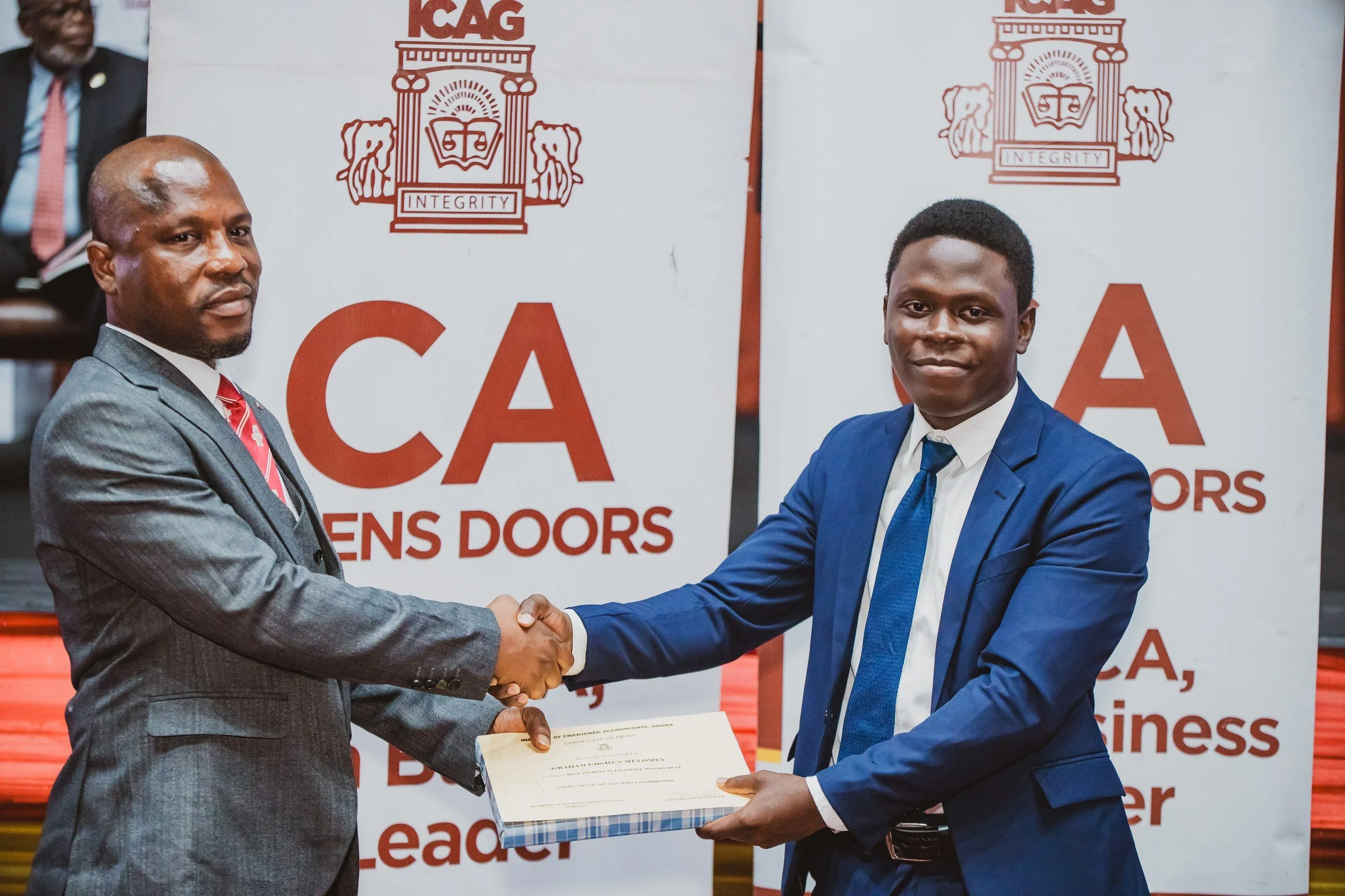 Graduate in a blue suit receiving a certificate with a handshake on stage, ICAG graduation, September 2025.