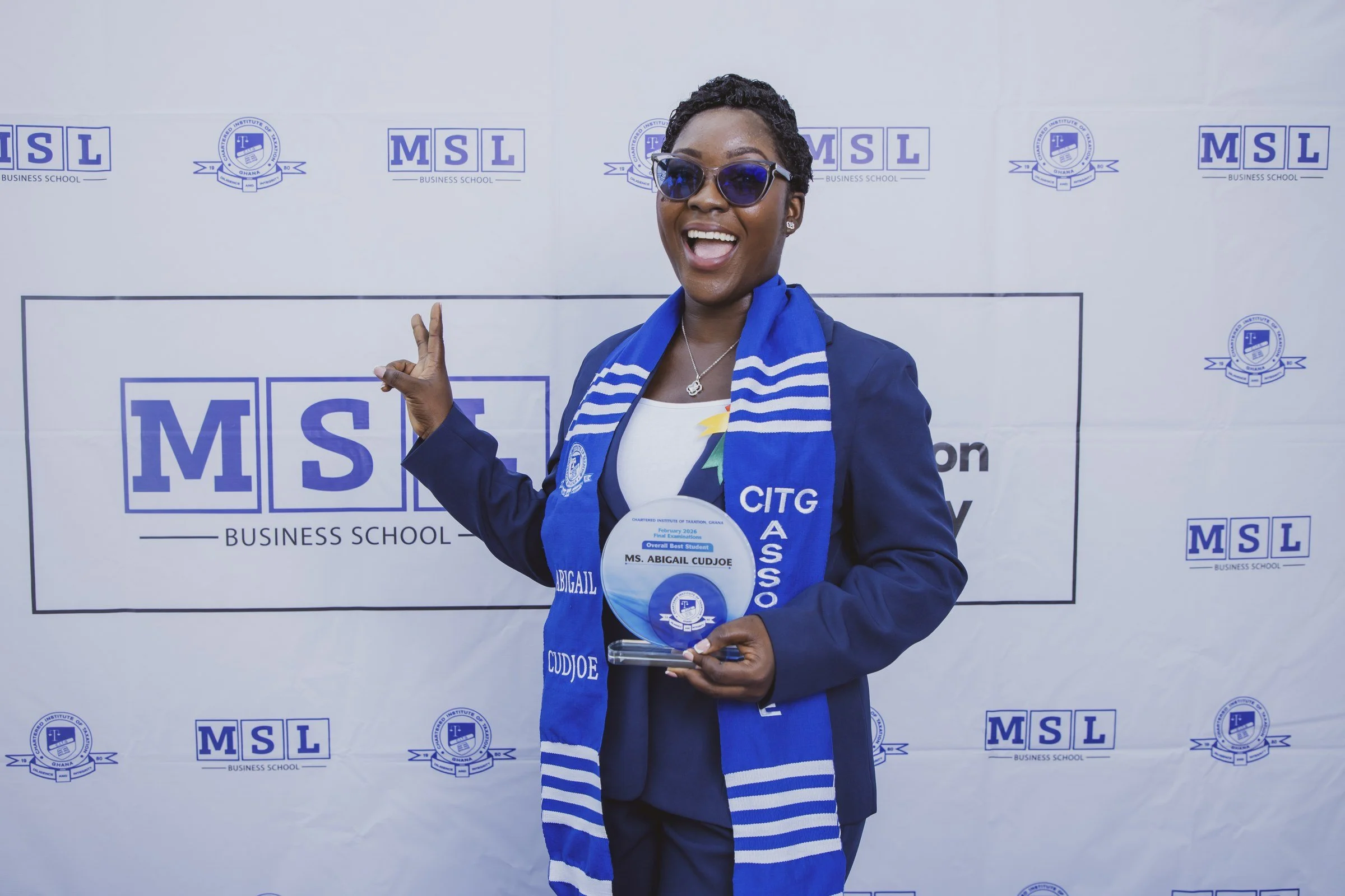Smiling CITG graduate holding a round trophy and raising a peace sign, CITG graduation, May 2026.