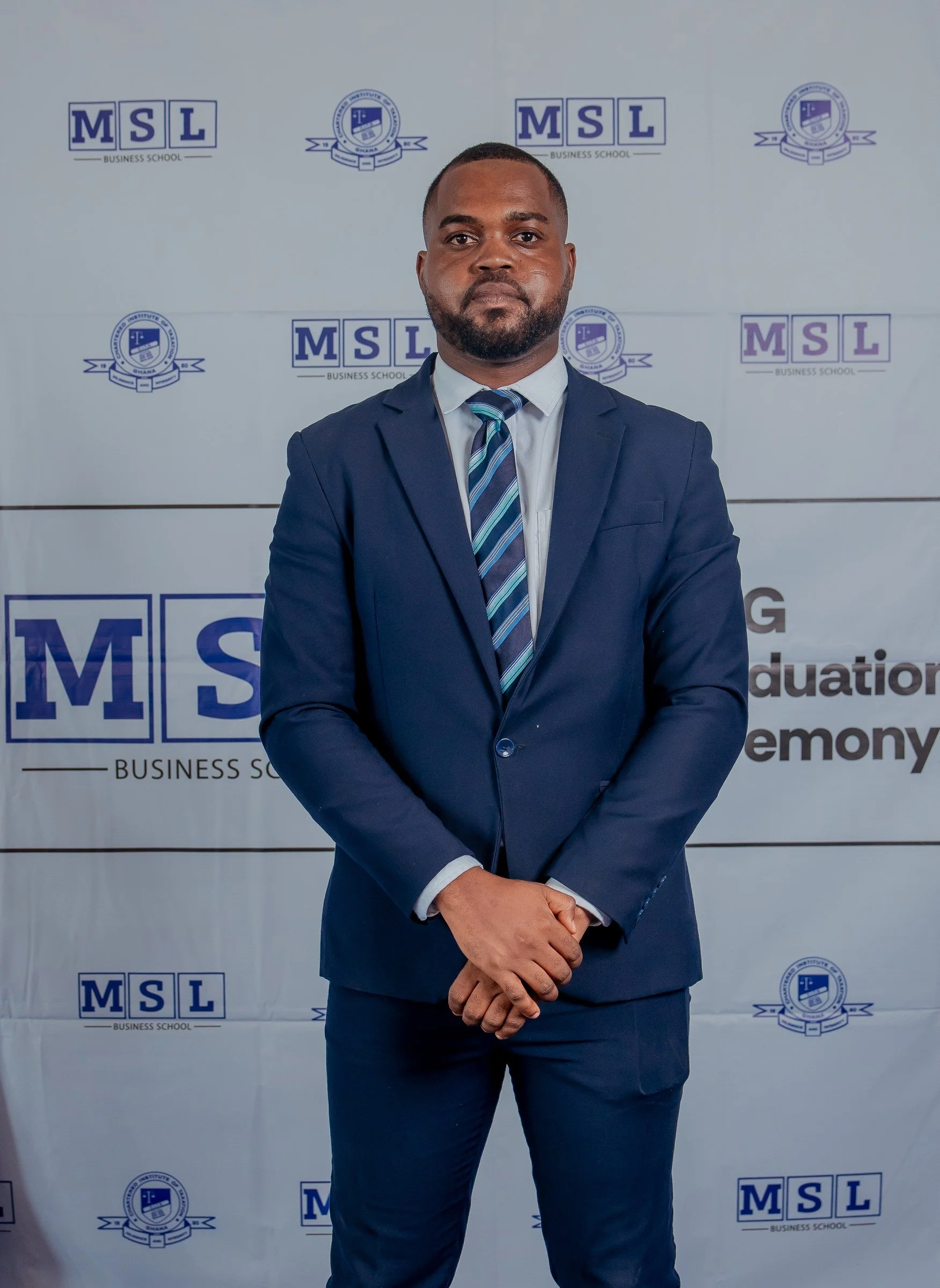 Portrait of a graduate in a navy suit and striped tie at the MSL backdrop, CITG graduation, December 2025.
