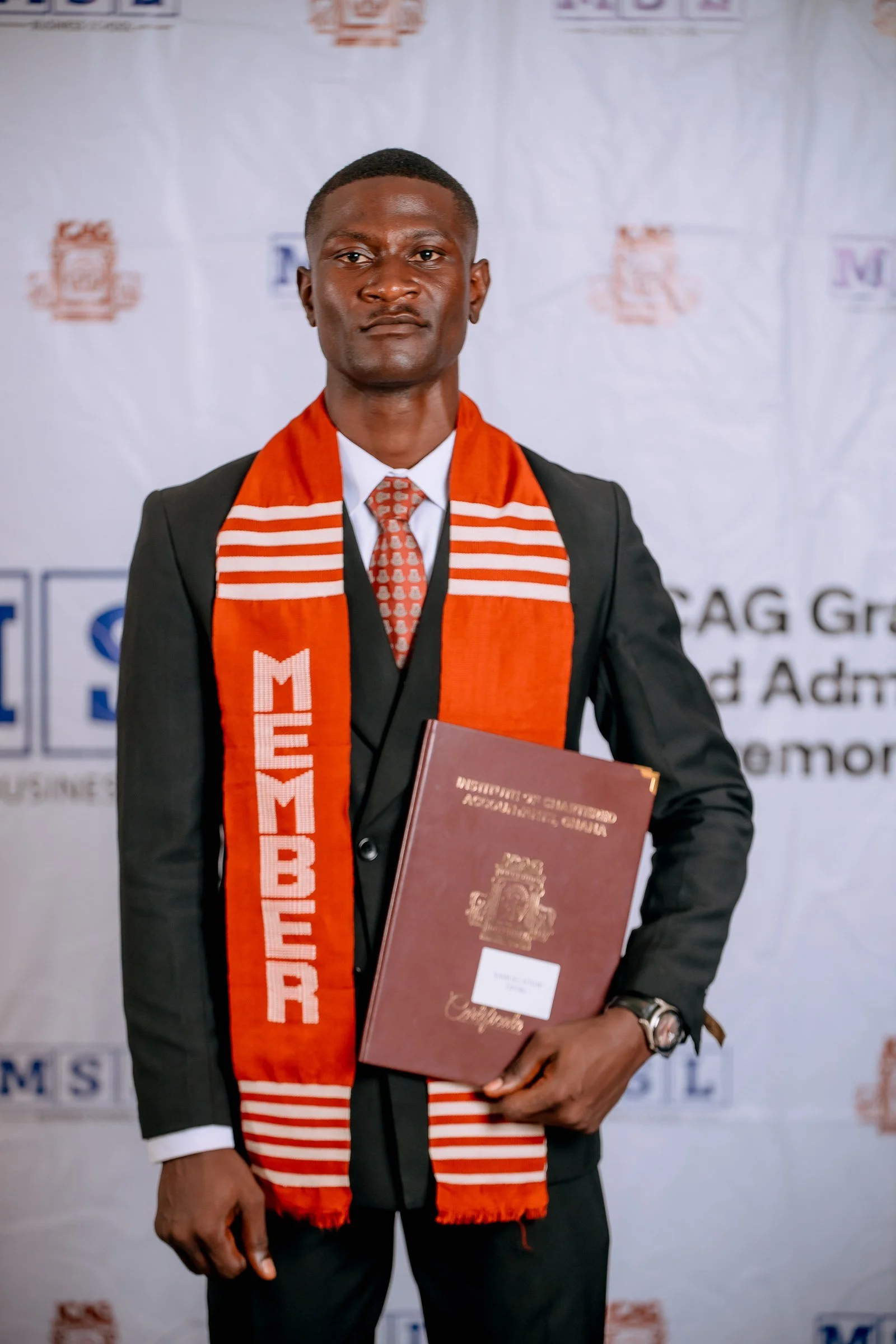 Graduate wearing glasses and a red ICAG stole holding his certificate folder, ICAG graduation, September 2025.