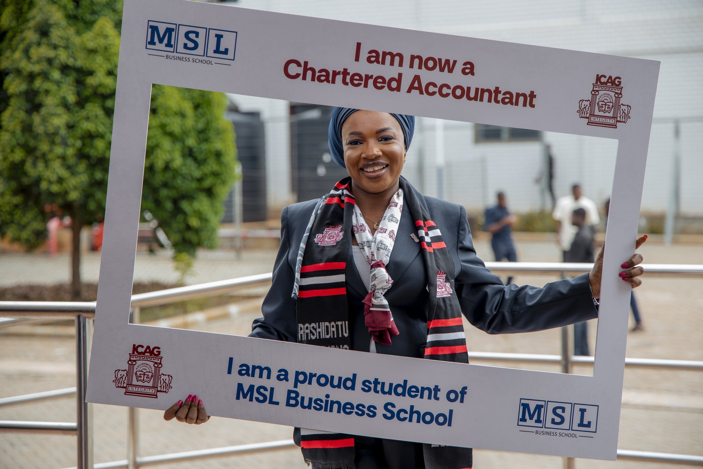 Smiling graduate in a headscarf holding an MSL Chartered Accountant photo frame outdoors, ICAG graduation, May 2025.