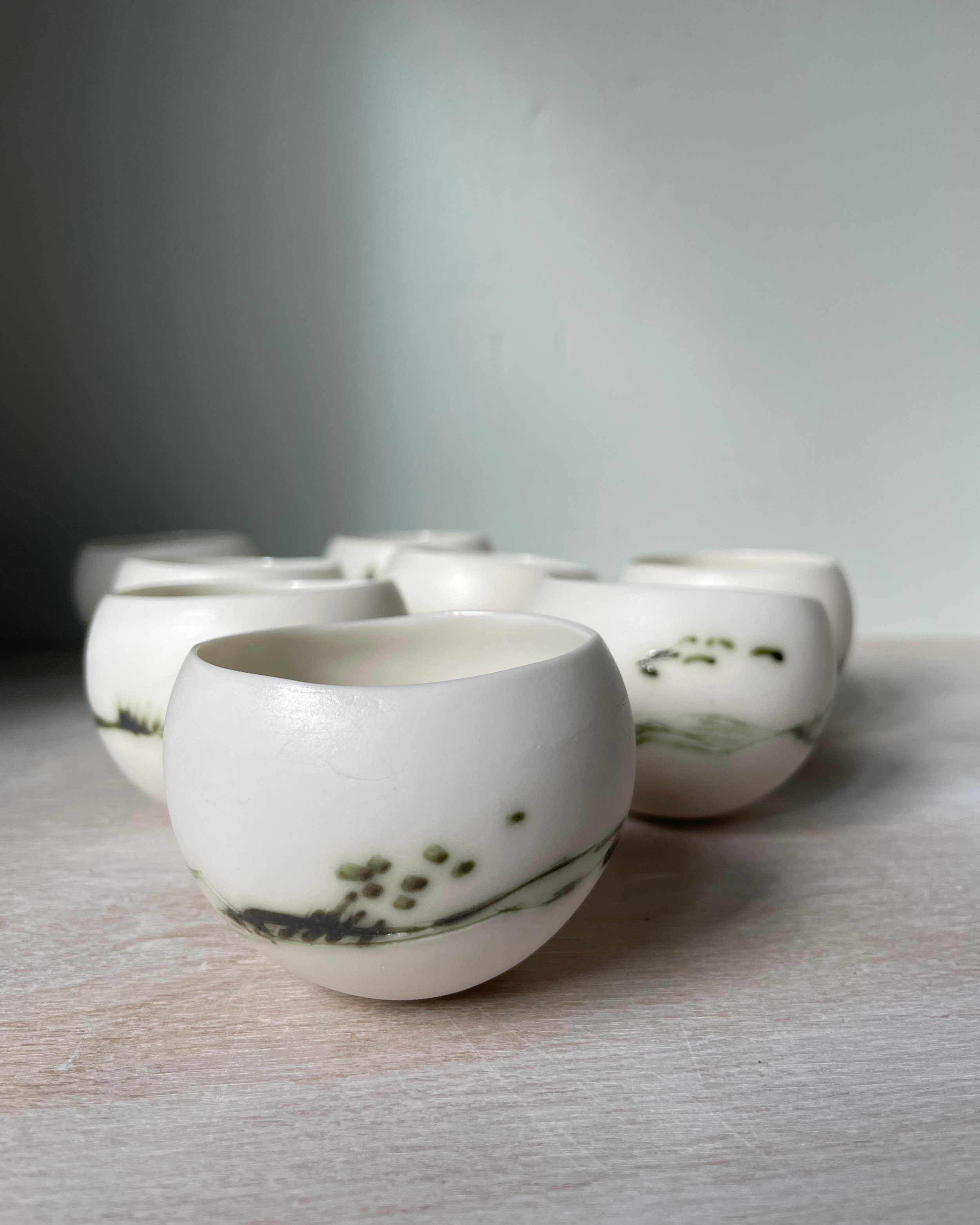Close-up of three handmade ceramic bowls with marble-like patterns, featuring shades of white, cream, and green, on a white background.