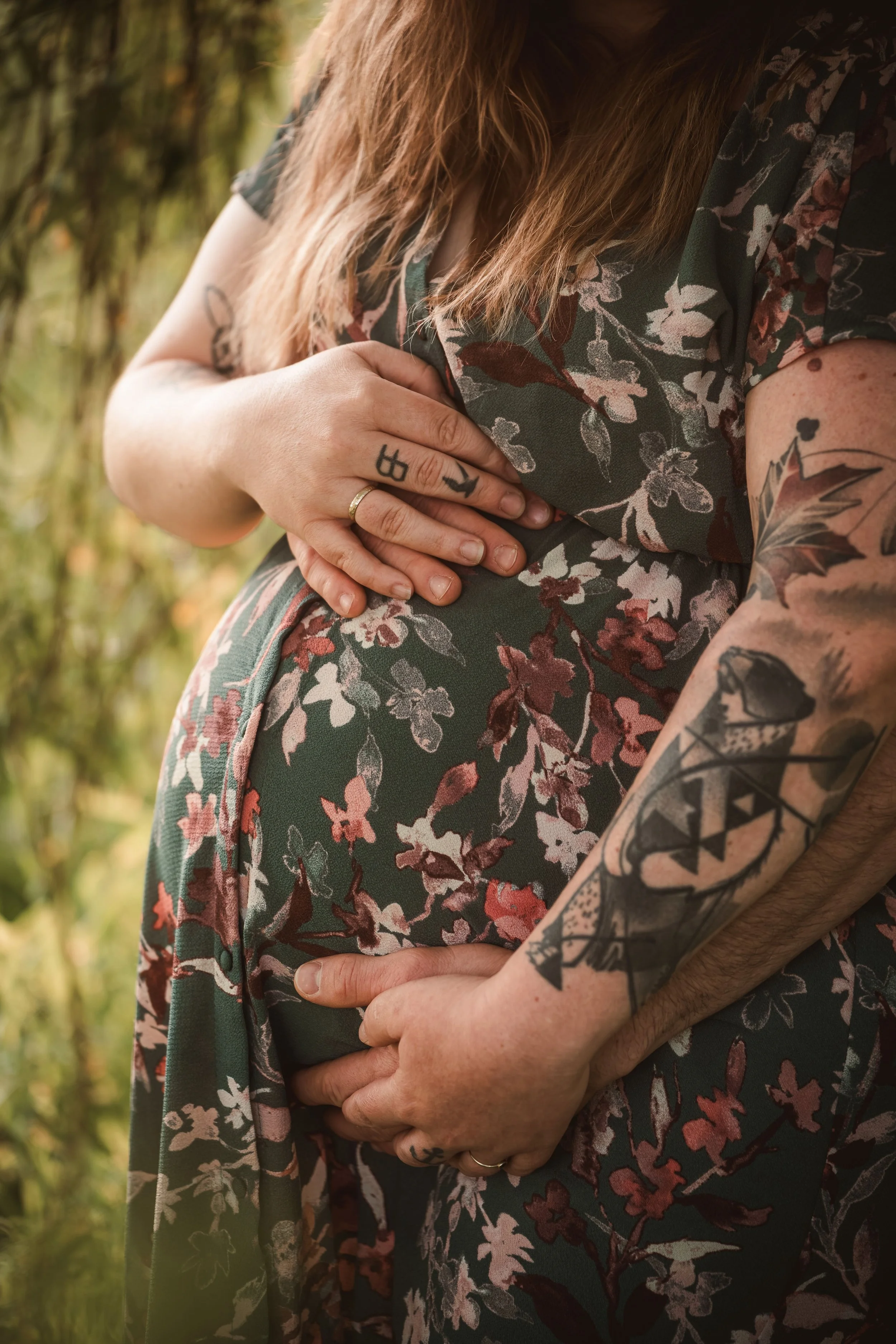 Nahaufnahme eines Paares, das sich umarmt. Der Fokus liegt auf ihren Armen, Tattoos und Händen, im Hintergrund unscharfe Naturumgebung.