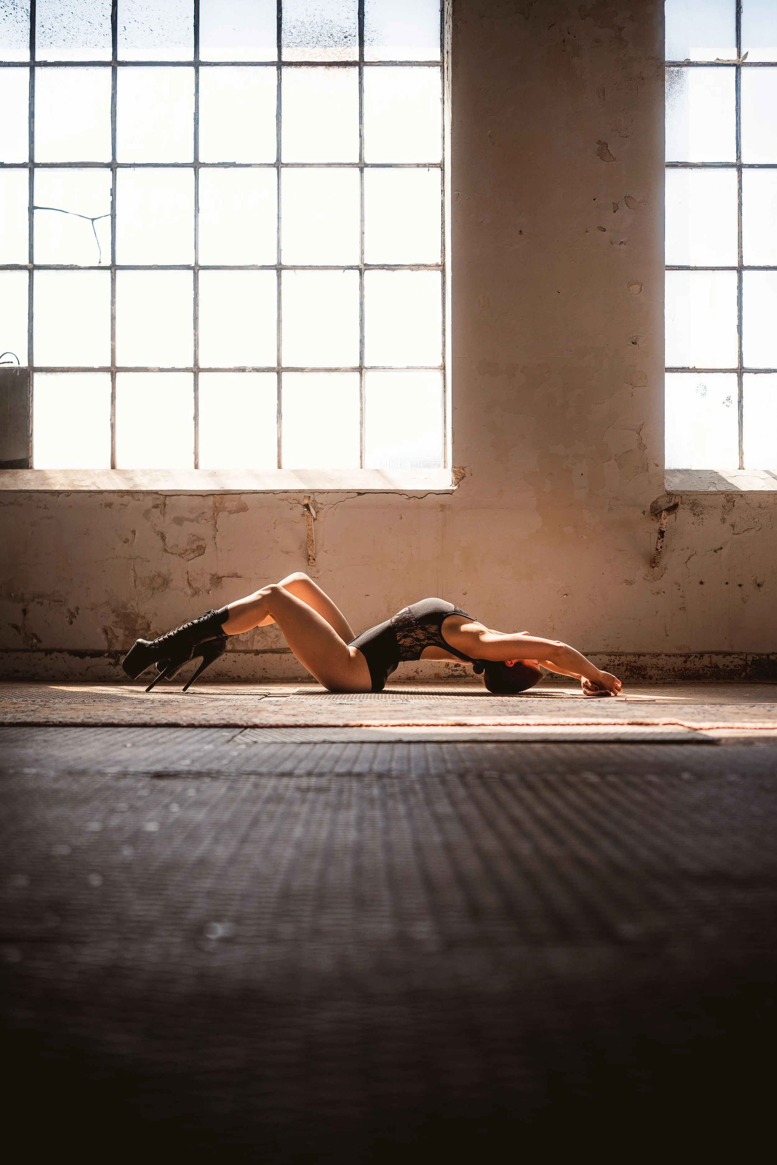 Eine Frau macht Yoga in einem abblätternden, industriellen Raum mit großen Fenstern, die viel Licht hineinlassen.