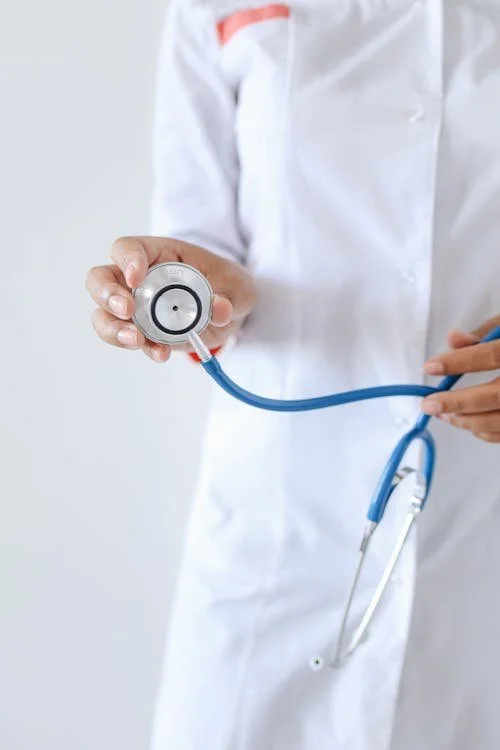 Healthcare professional in a white coat holding a stethoscope toward the camera.